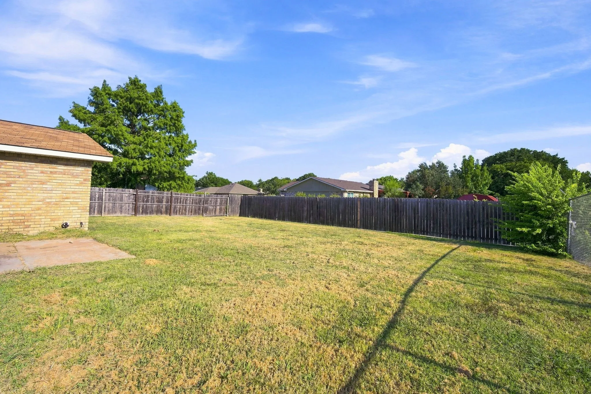 Expansive backyard with mature shade trees, manicured lawn, and privacy fencing