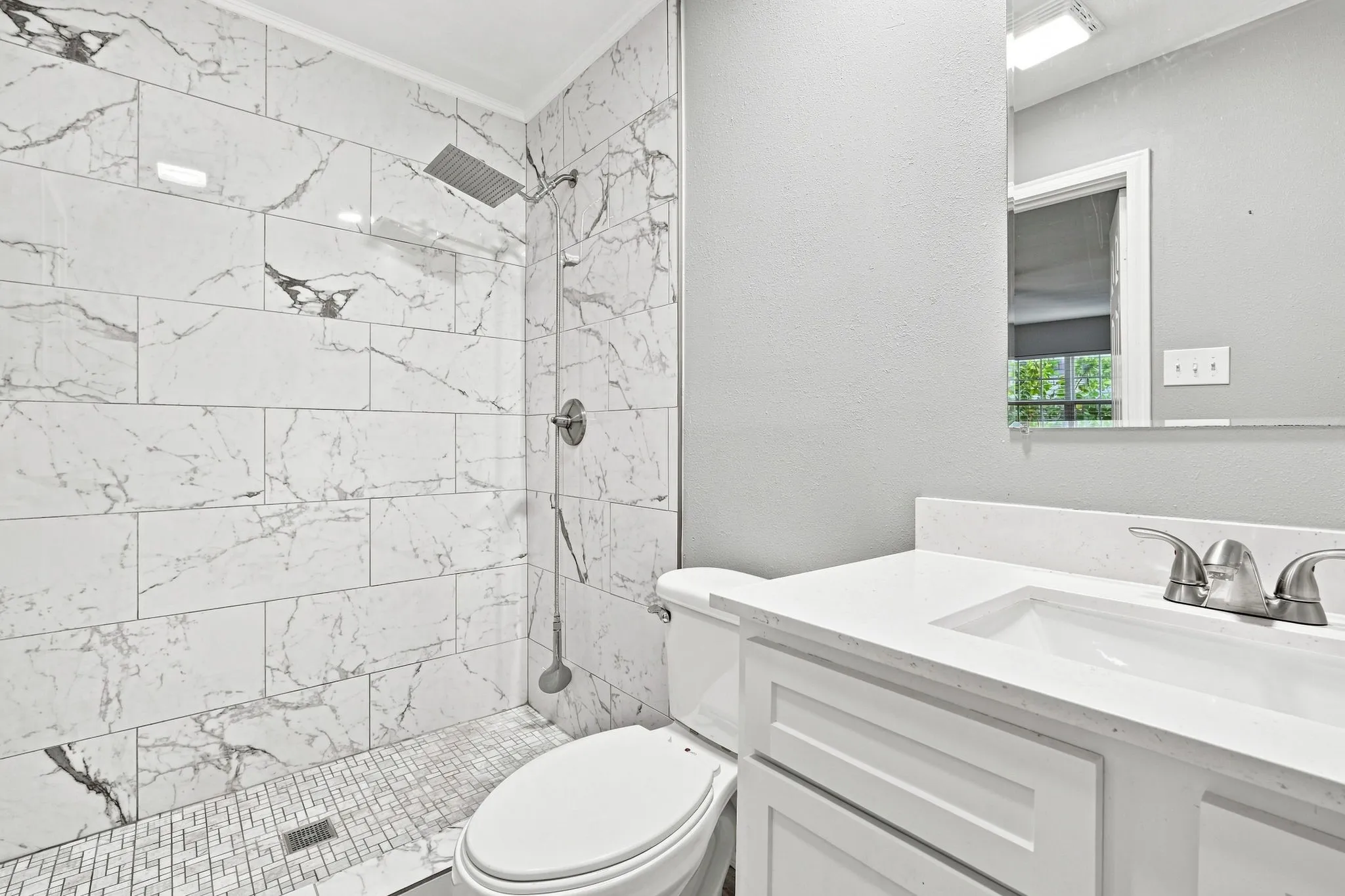 Walk-in shower with large-format tile surround, rain shower head, hand-held shower fixture, and mosaic tile flooring