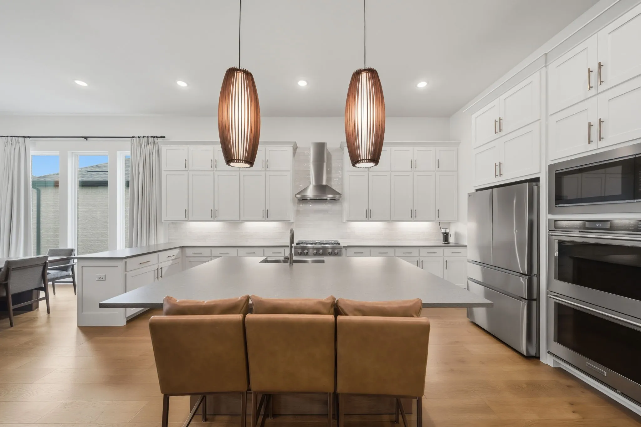 Spacious kitchen featuring an expansive center island, white cabinetry, stainless steel appliances, and wood-finish flooring
