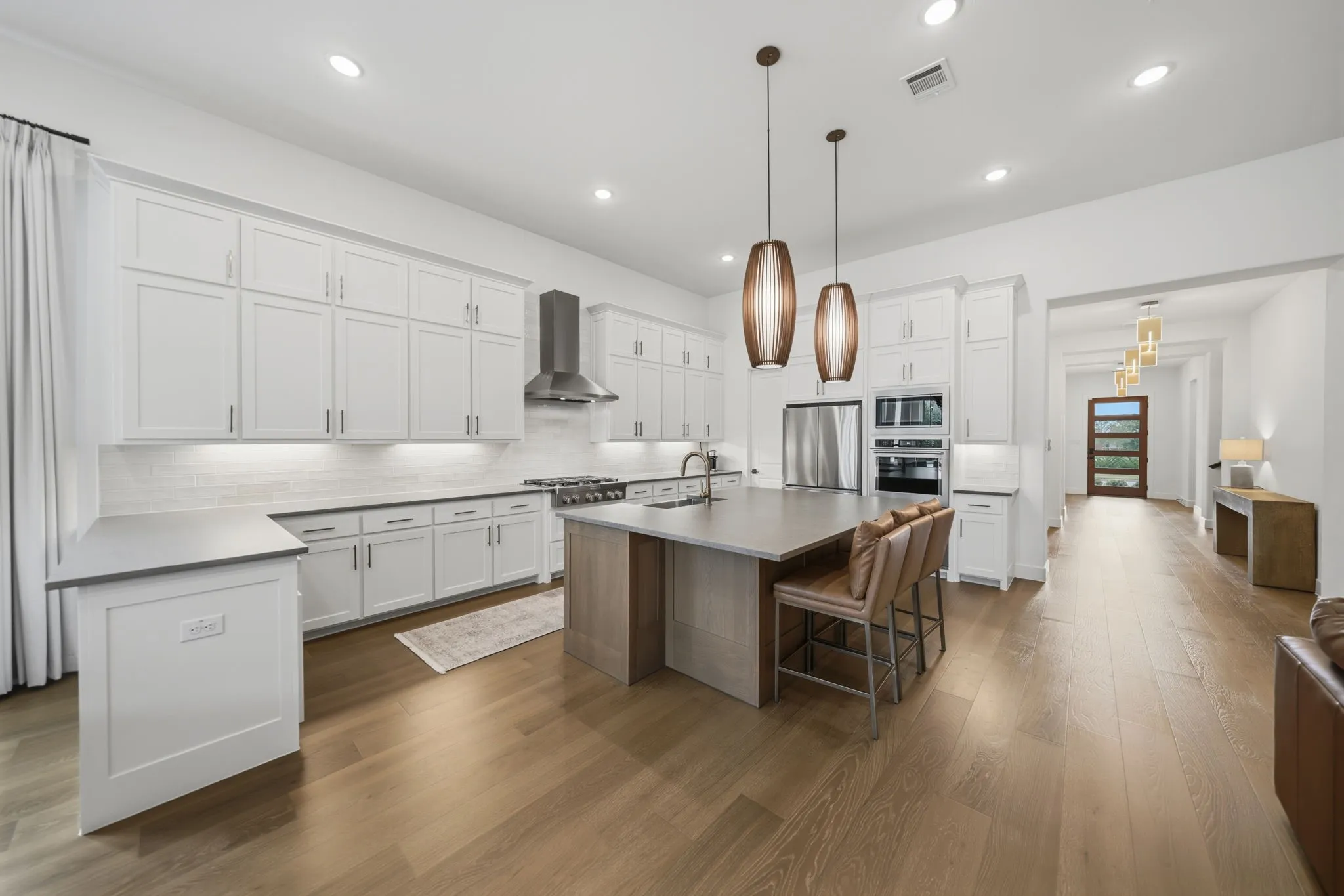 Gourmet kitchen with white shaker cabinetry, stainless steel appliances, a center island with seating, and wood-finish flooring