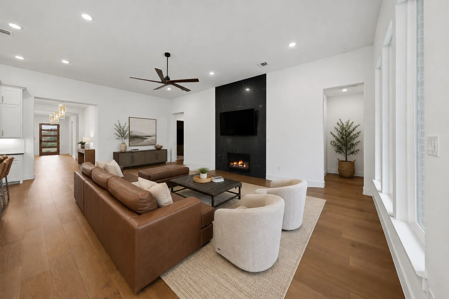 Spacious living area featuring high ceilings, wood-finish flooring, a contemporary fireplace with a dark stone-finish surround, and recessed lighting