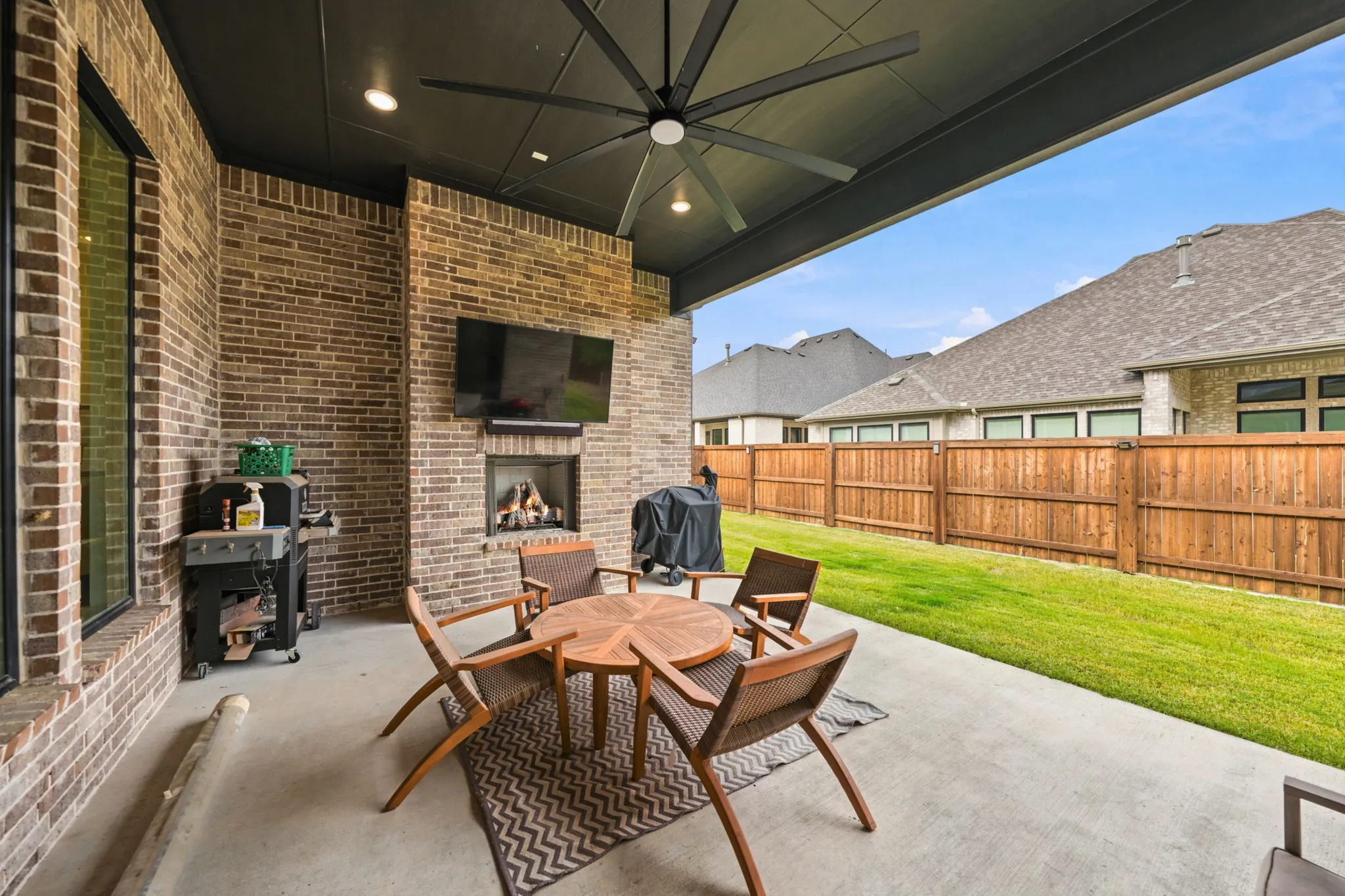 Covered patio featuring brick construction, a built-in fireplace, a ceiling fan, and a concrete slab
