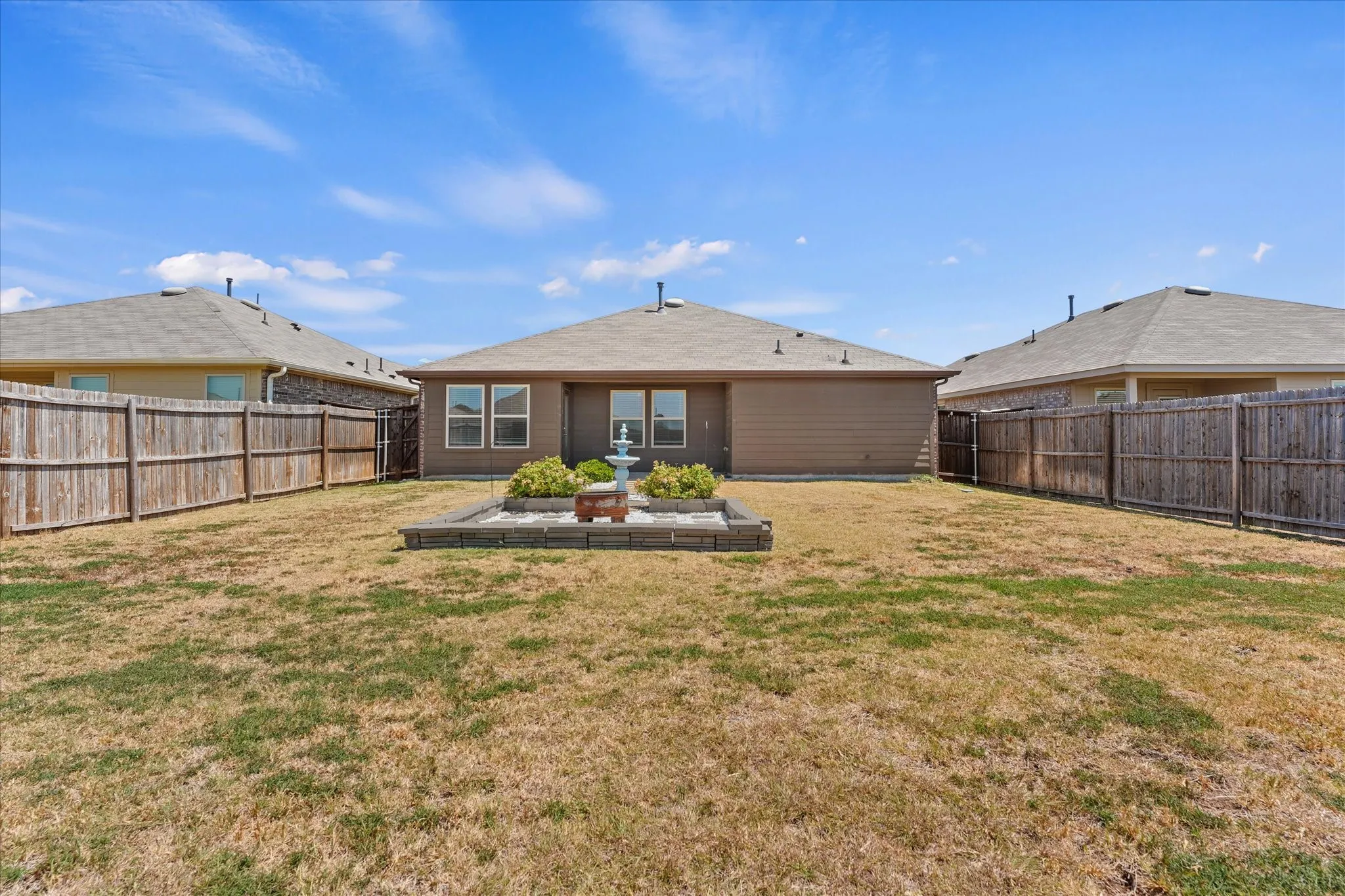 Spacious backyard with expansive manicured lawn, mature landscaping featuring central planting beds, and fully fenced perimeter