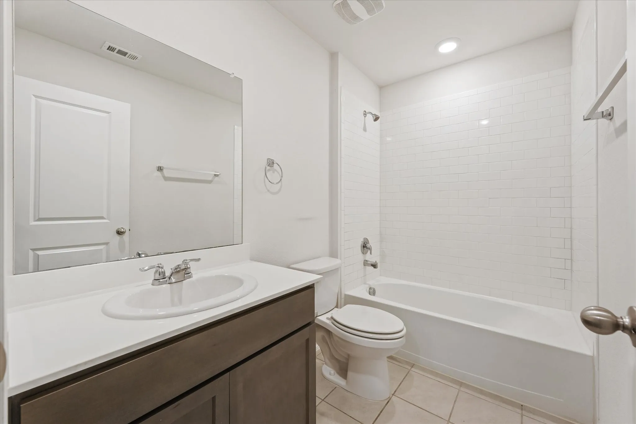 Full bathroom featuring a rectangular vanity mirror, single-basin sink with a chrome faucet, dark wood-finish vanity with storage, and a shower-tub combination with white subway tile surround