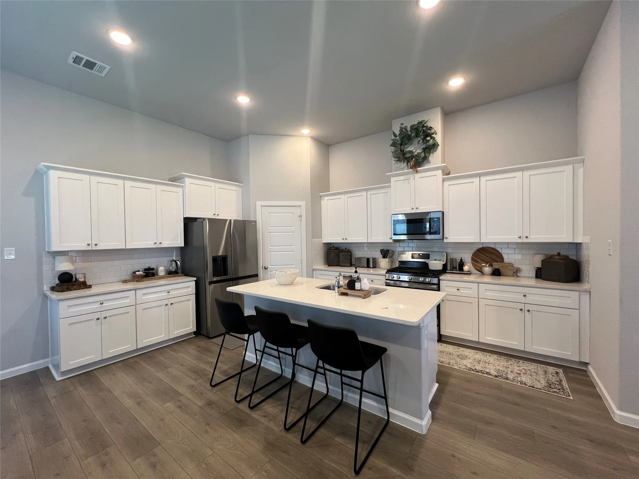 Kitchen featuring appliances with stainless steel finishes, backsplash, a breakfast bar area, white cabinetry, and dark wood-type flooring