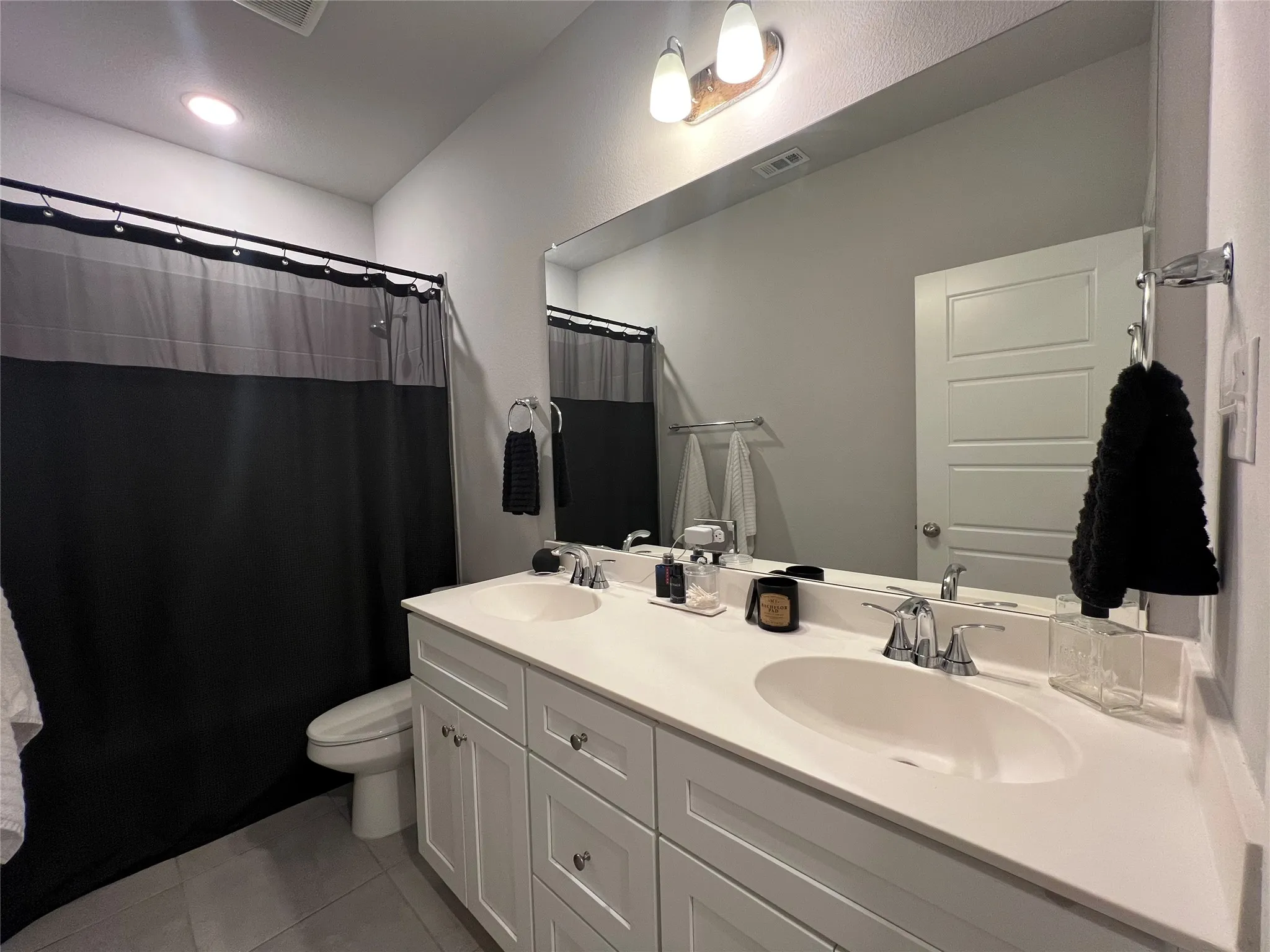 Bathroom with double vanity, tile patterned floors, and a shower with curtain