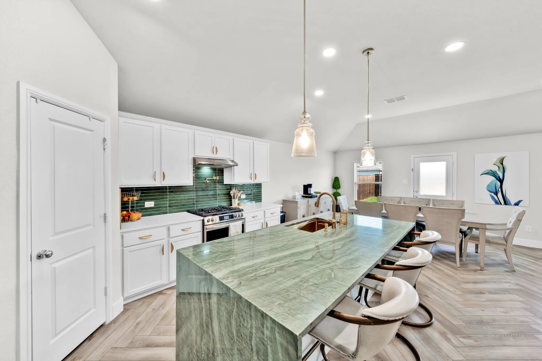 Kitchen island with a waterfall edge, white cabinetry, green tile backsplash, stainless steel range, and two pendant lights