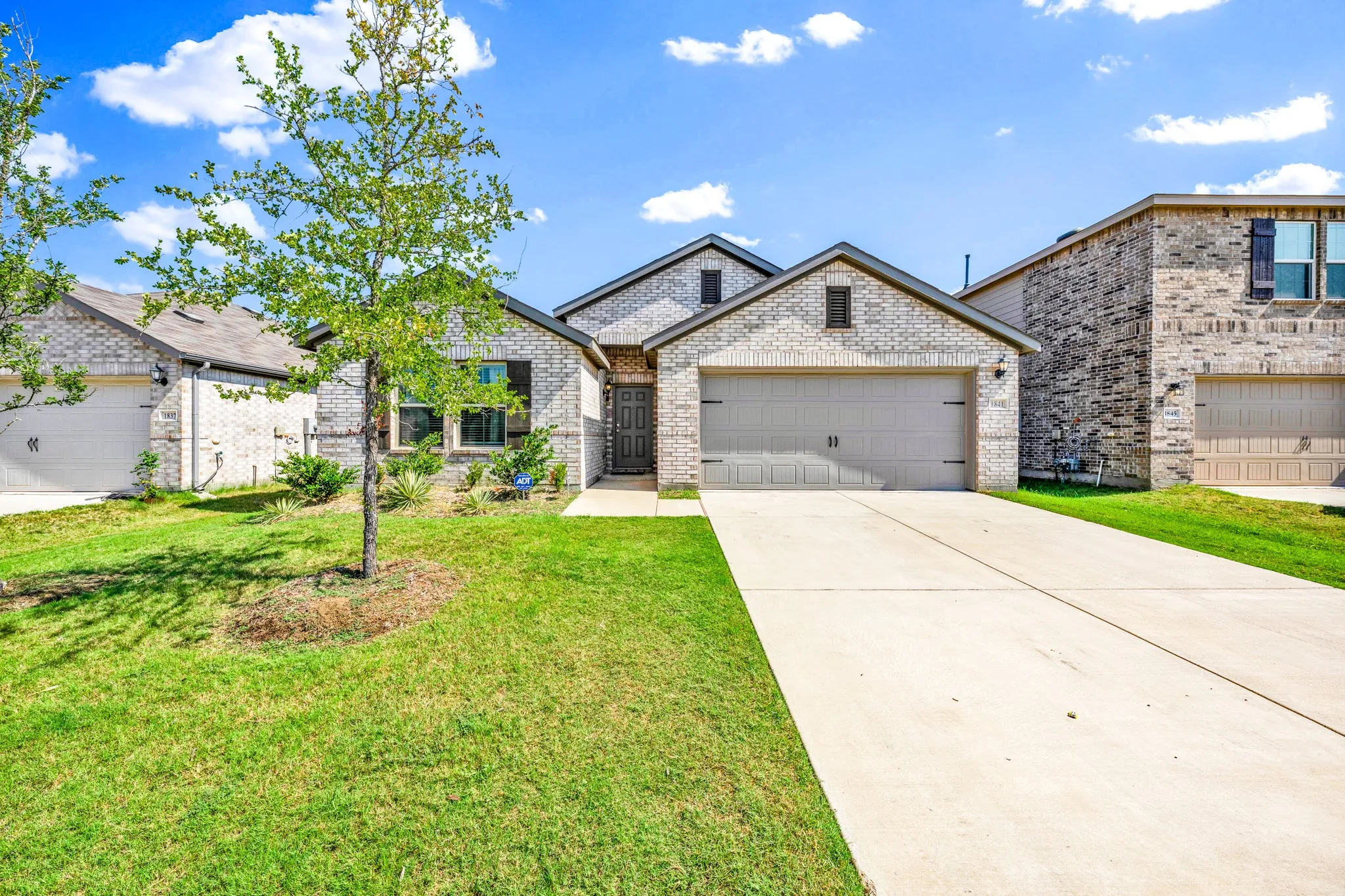 Brick exterior, attached two-car garage, concrete driveway, front yard landscaping, and pitched roofline