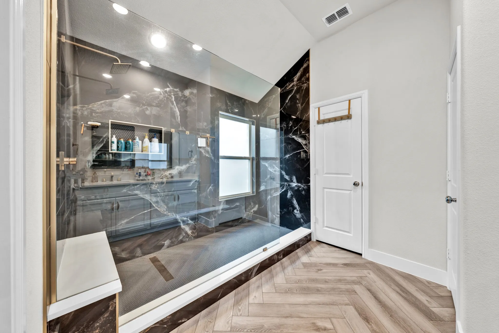 Spacious walk-in shower with frameless glass enclosure and dark marble-look porcelain tile