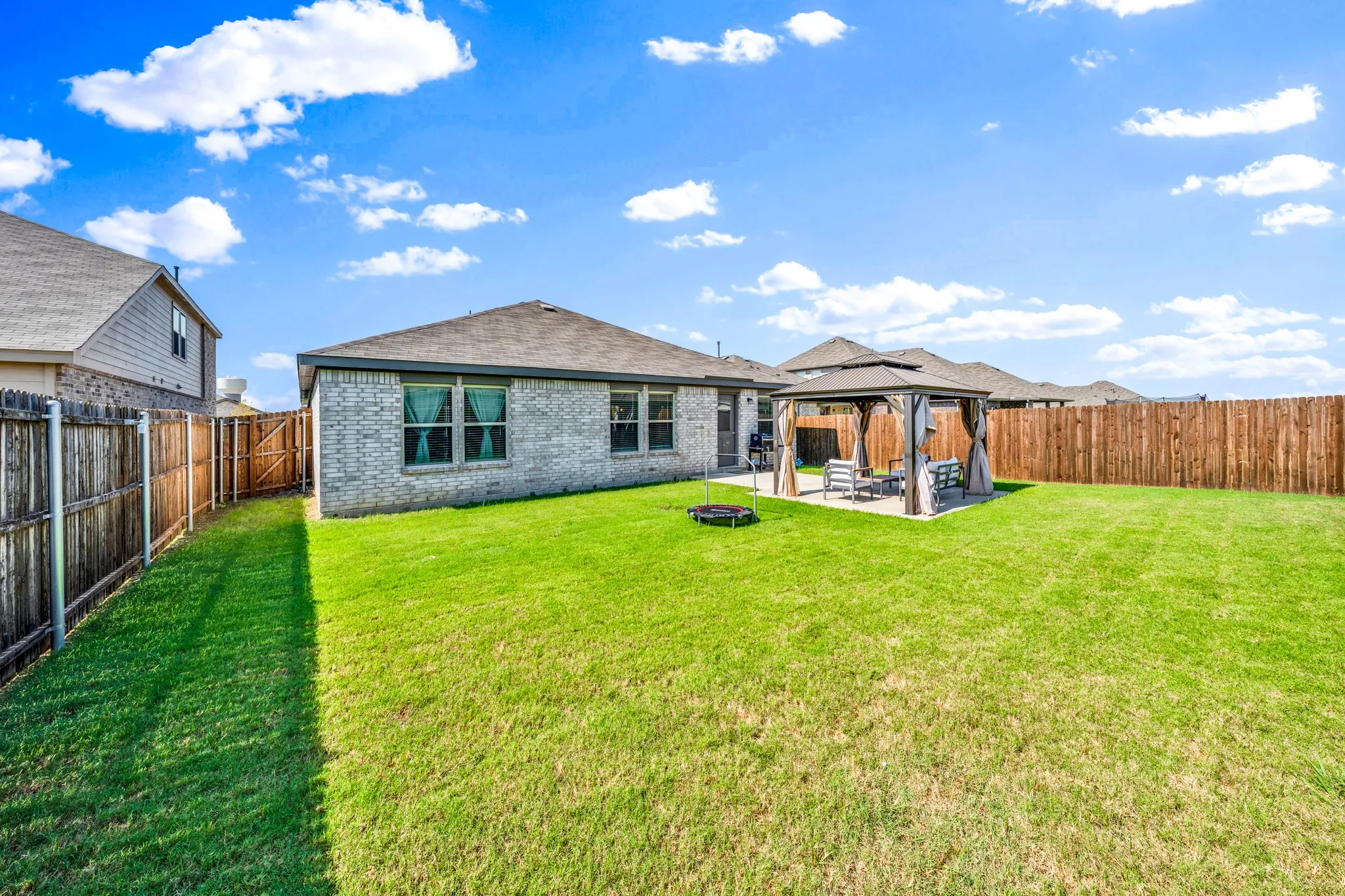 Expansive backyard featuring a manicured lawn, full privacy fencing, and a built-in paved patio with a gazebo