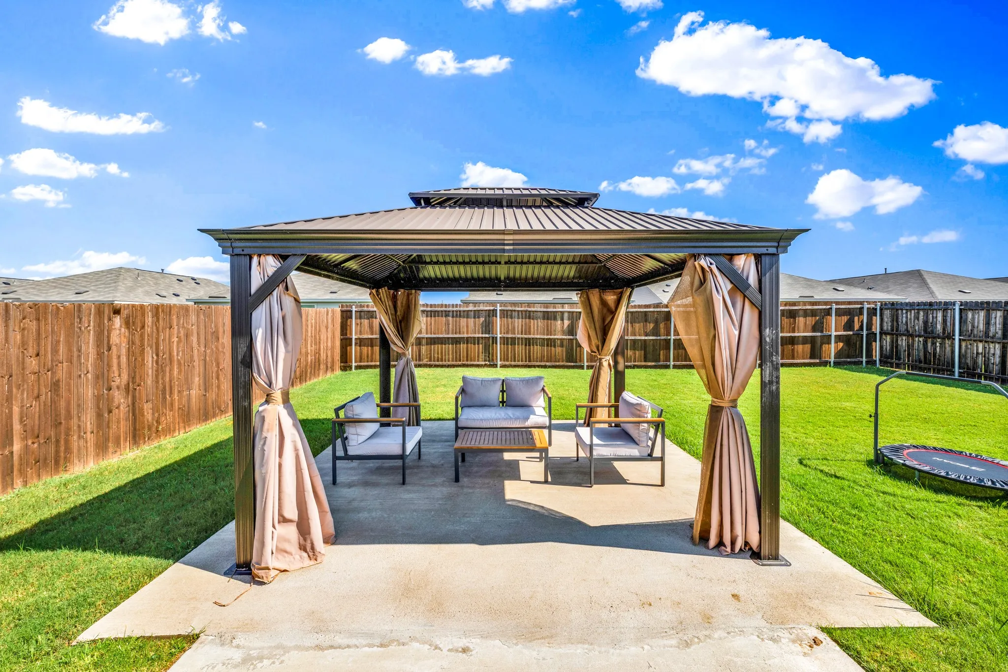 Private backyard featuring a large concrete patio, a metal gazebo with privacy drapes, and a wood privacy fence