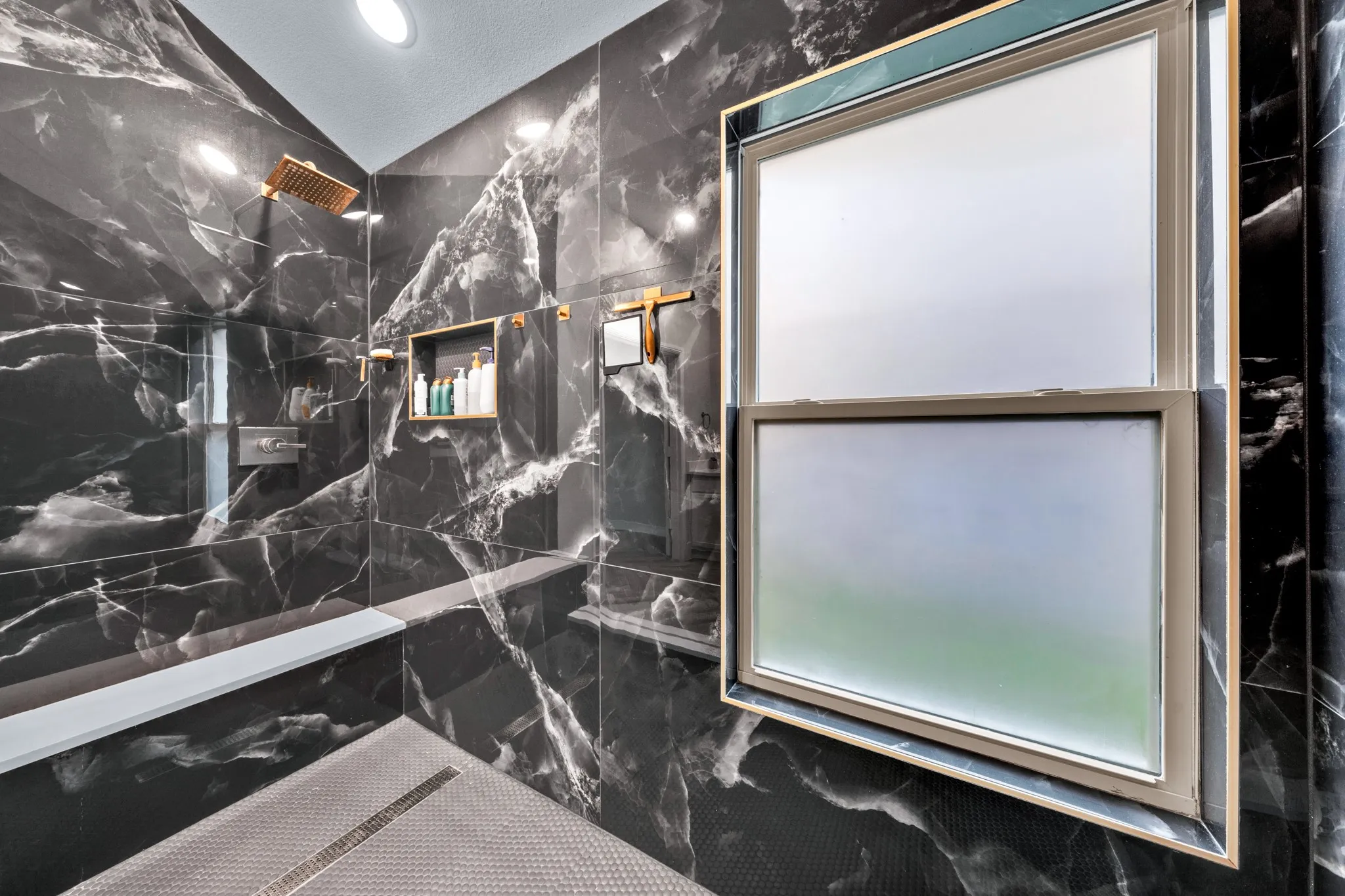 Black porcelain tiled shower enclosure with a built-in bench, recessed shelf, and bronze-finish fixtures