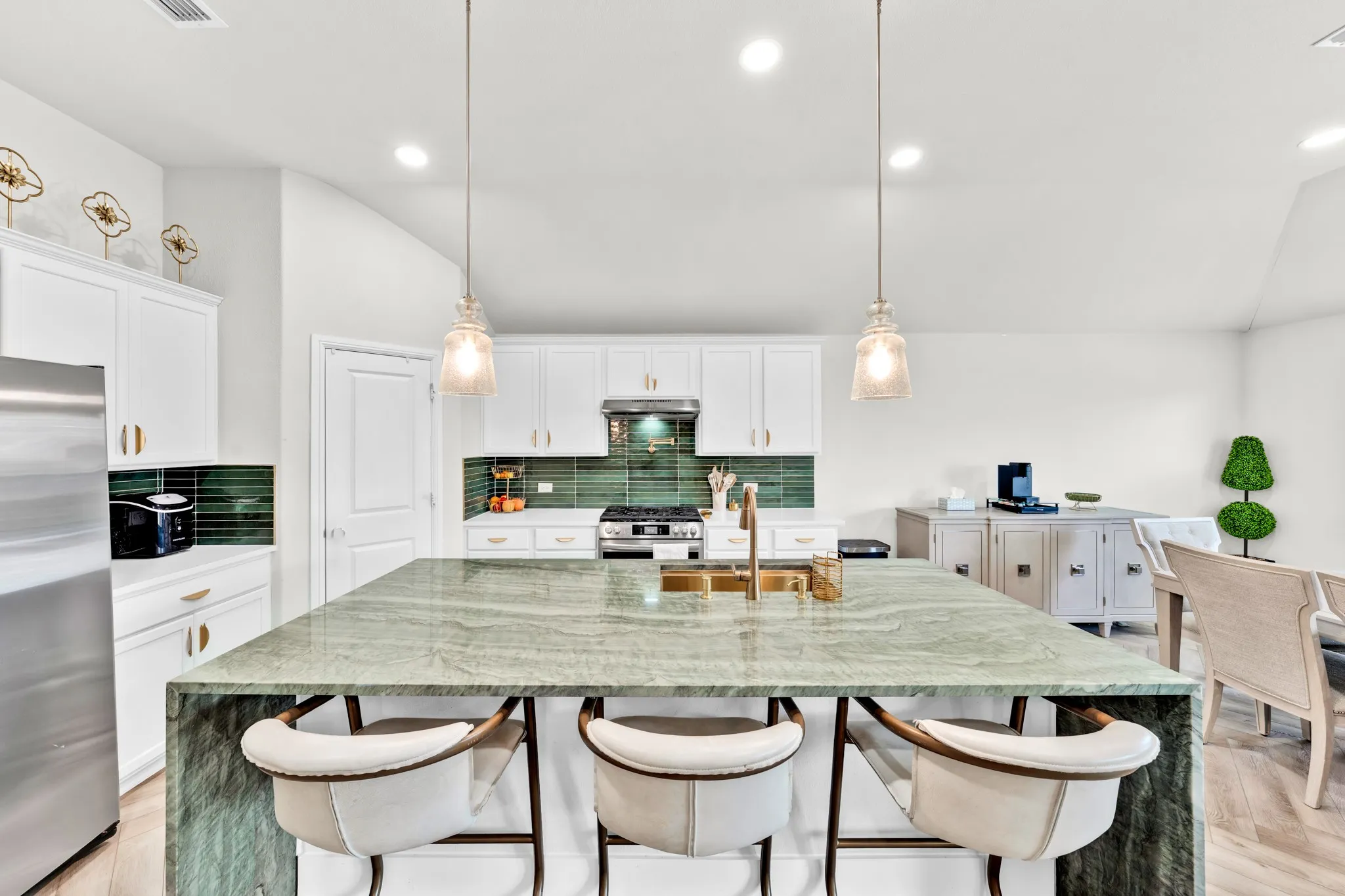 Kitchen featuring a waterfall-edge island, white cabinetry, a green tiled backsplash, stainless steel appliances, and pendant lighting