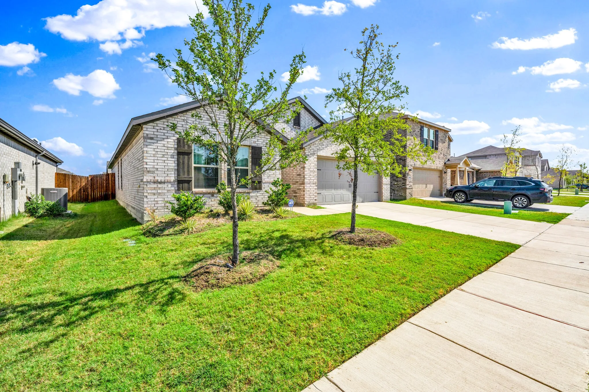 Brick and stone facade, attached two-car garage, concrete driveway, manicured lawn, and mature landscaping
