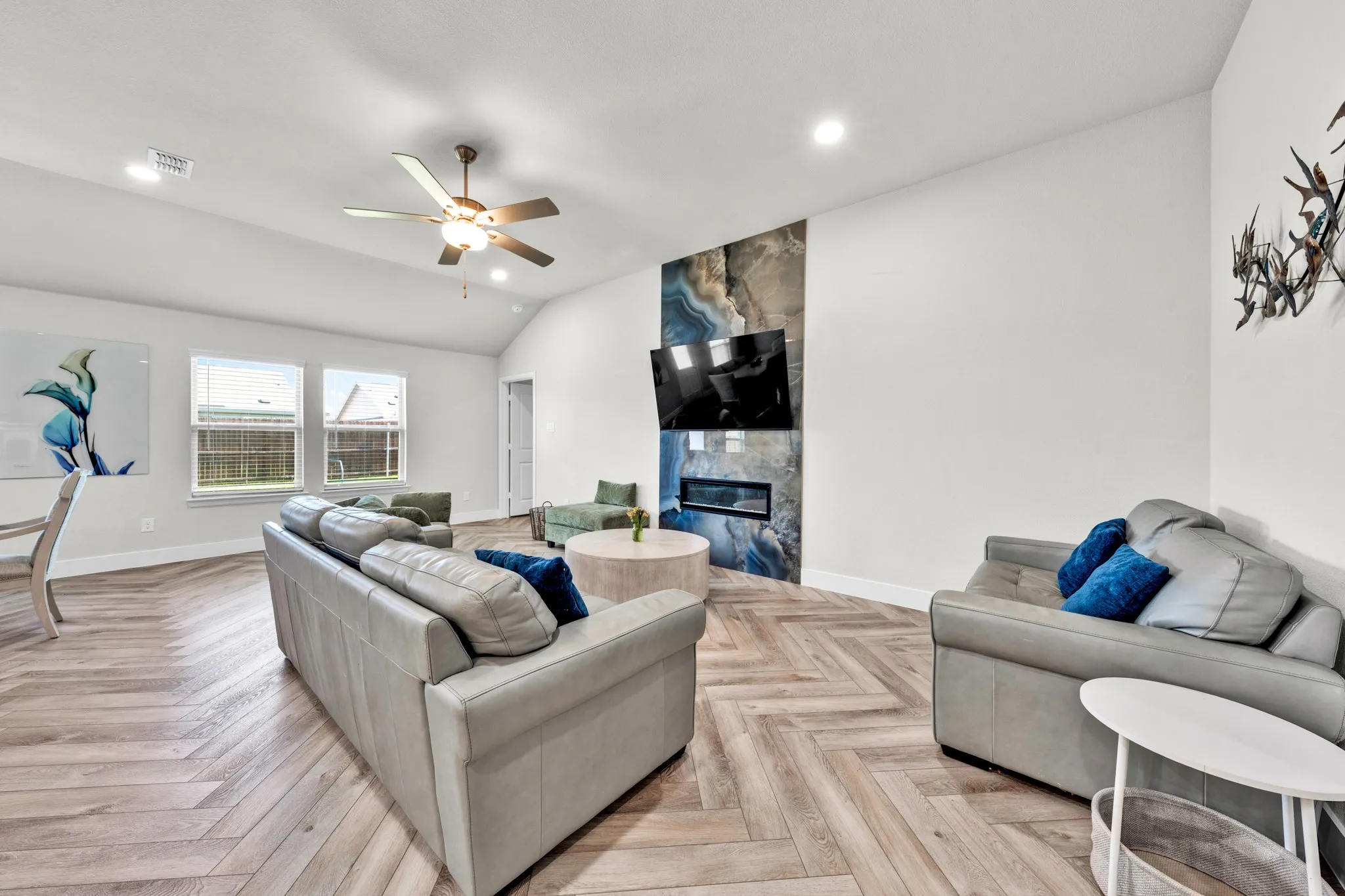 Vaulted ceiling with a ceiling fan, wood-finish herringbone flooring, a built-in electric fireplace, and a porcelain slab feature wall