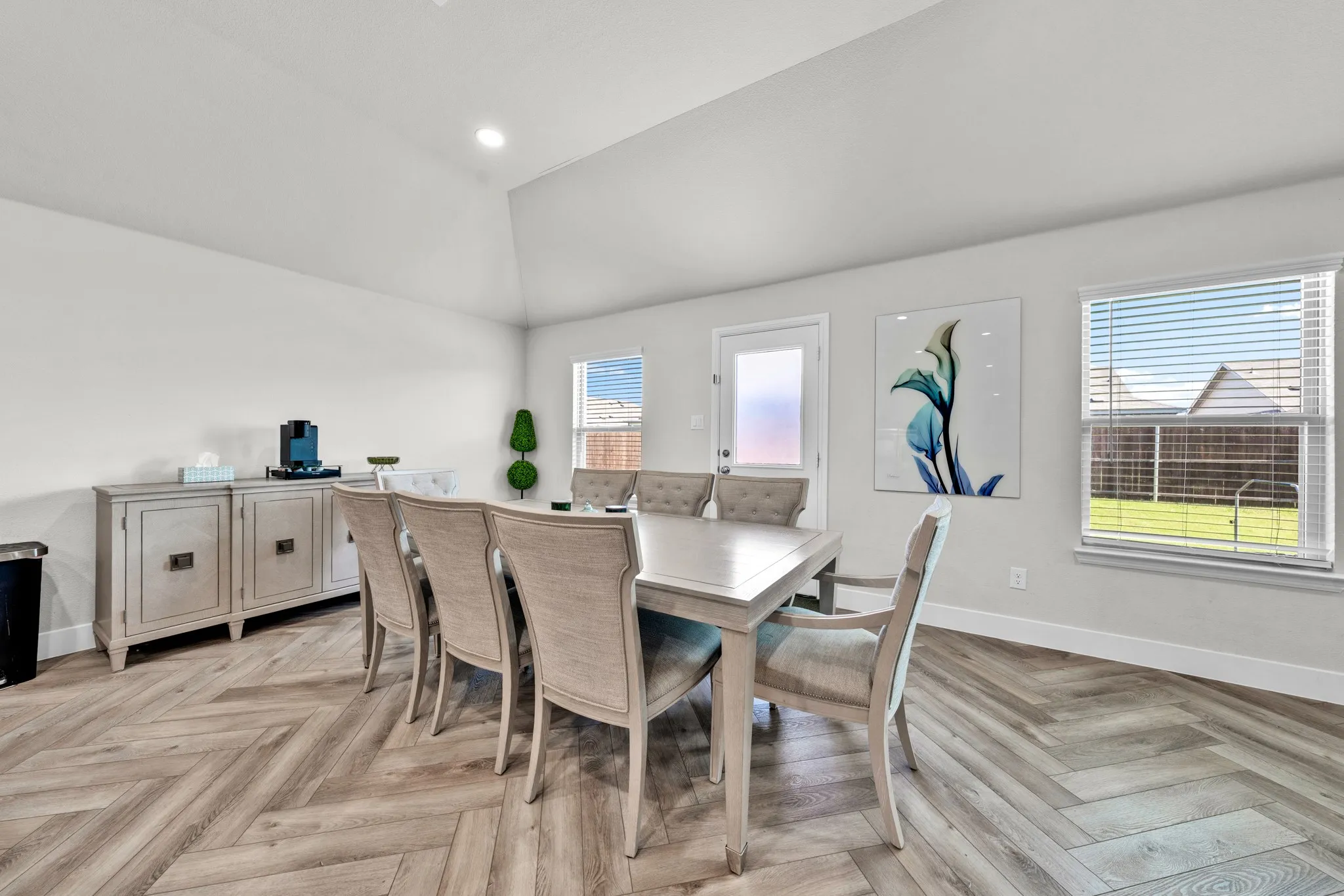 Vaulted ceiling with recessed lighting, wood-finish flooring in a herringbone pattern, white walls, and a glass-paneled door