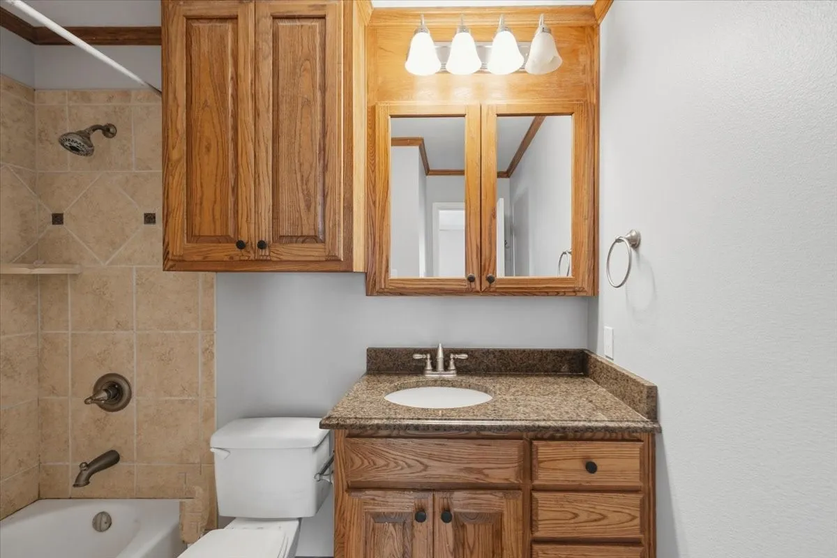 Bathroom featuring a tub with tile surround, wood-finish vanity with a granite-style countertop, integrated sink, and an overhead medicine cabinet with mirrored doors