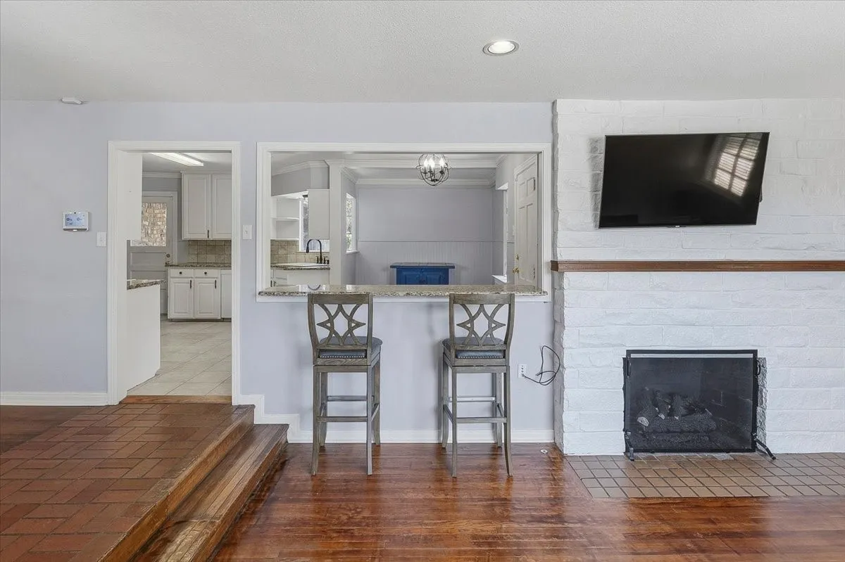 Wood-finish flooring throughout, white brick fireplace with a wood mantle, recessed lighting, and a built-in bookshelf