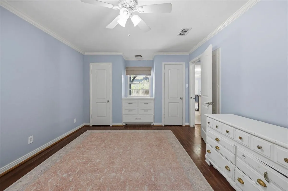 Wood-finish flooring, ceiling fan, crown molding, built-in dresser, and painted walls