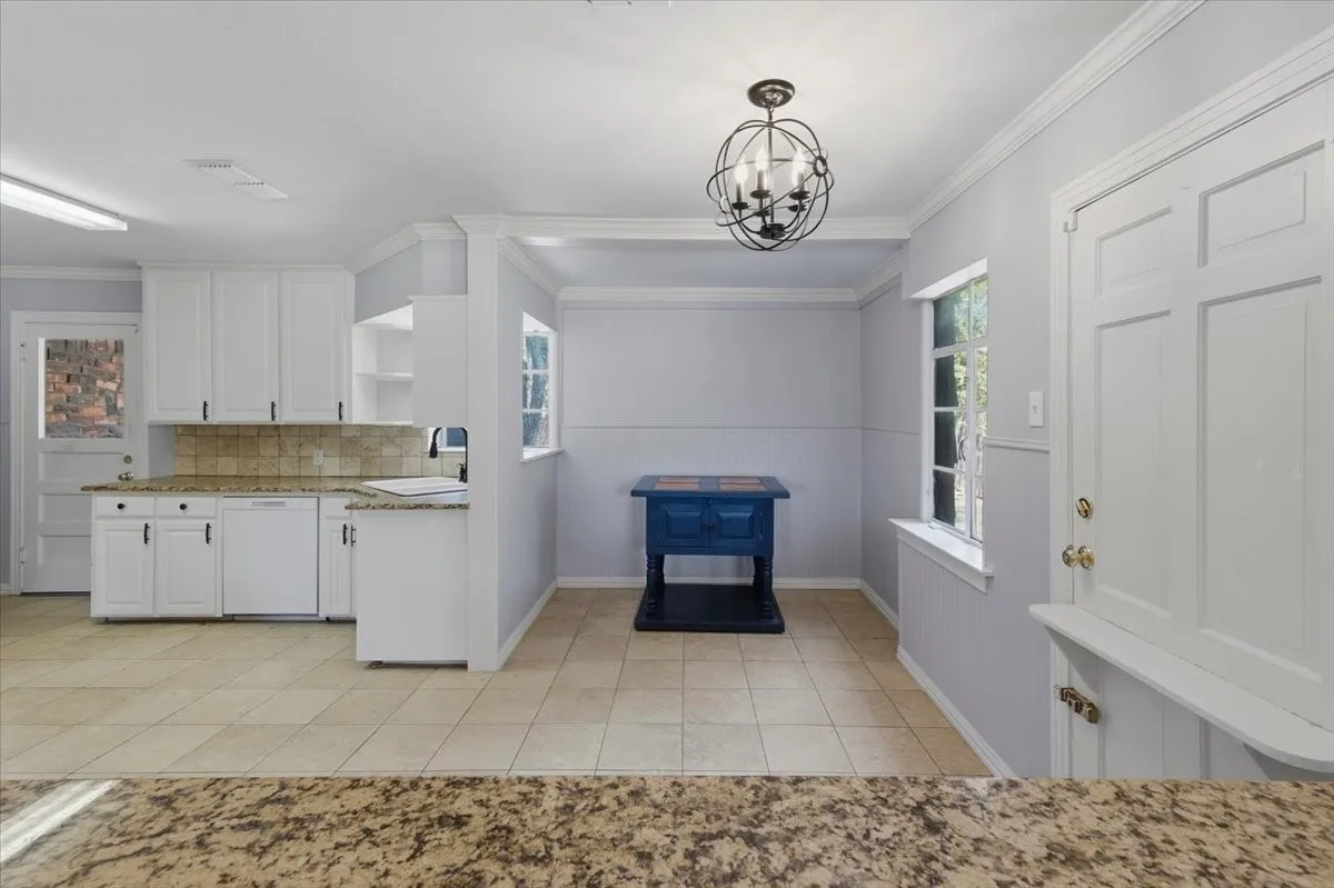 White kitchen cabinetry with black hardware, stone countertops, a tiled backsplash, and light-colored tile flooring