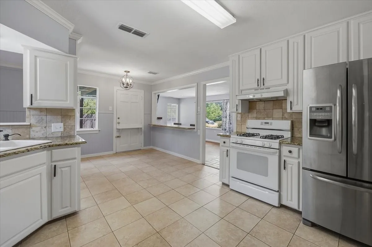 Kitchen featuring white cabinetry, light-toned tile flooring, granite-style countertops, stainless steel refrigerator, and white gas range with coordinating hood