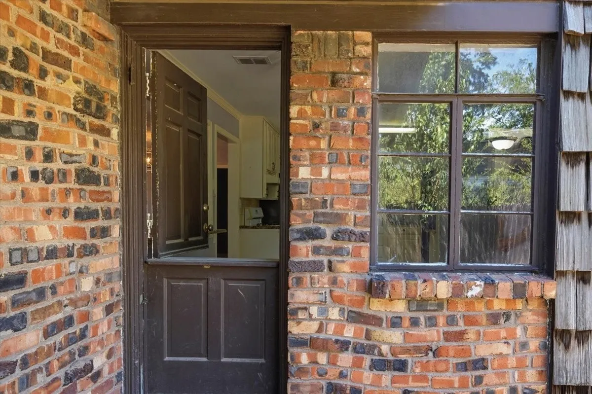Charming brick entry featuring a paneled wood door with transom window, complemented by multi-pane casement windows framing natural light