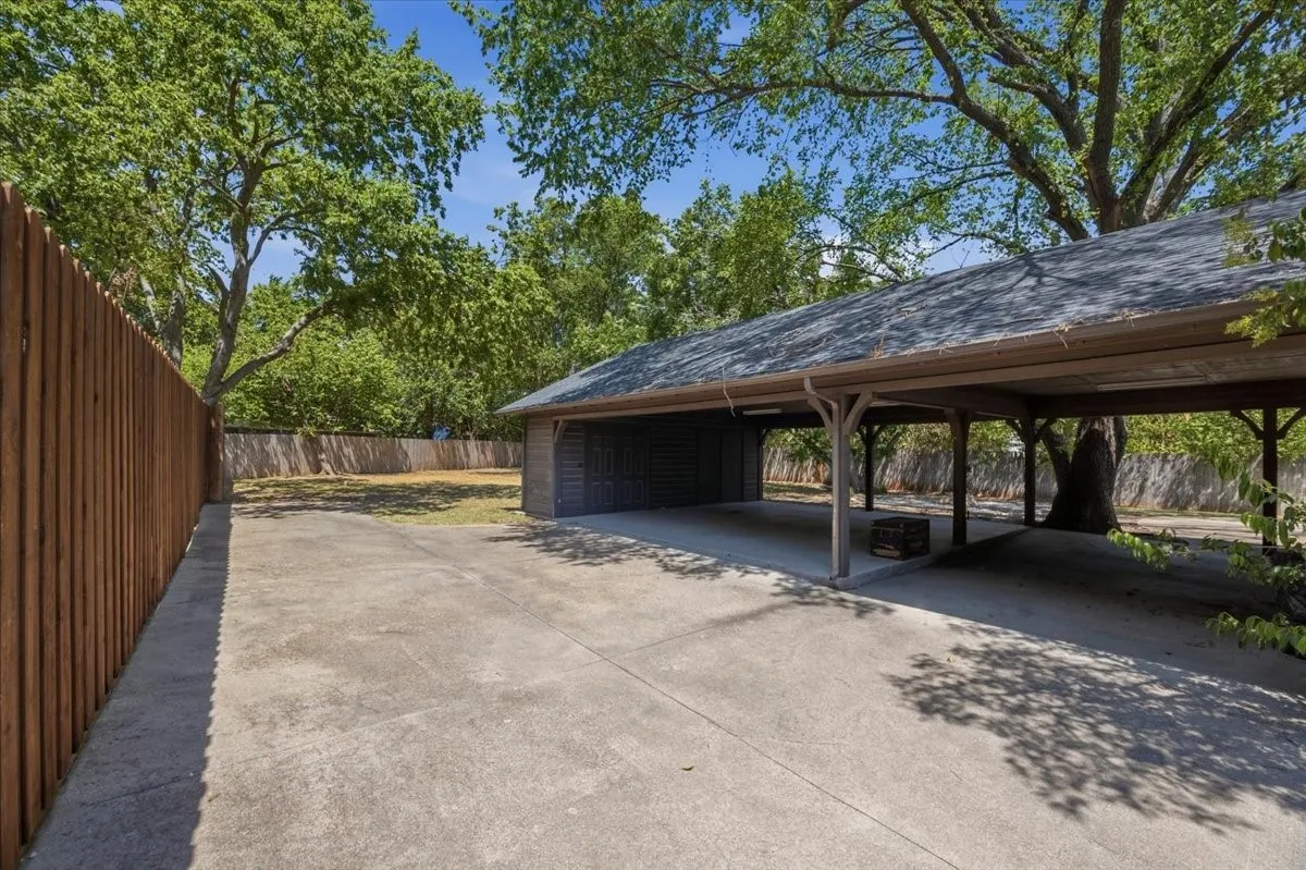 Expansive concrete driveway leading to a multi-vehicle carport with an attached storage shed