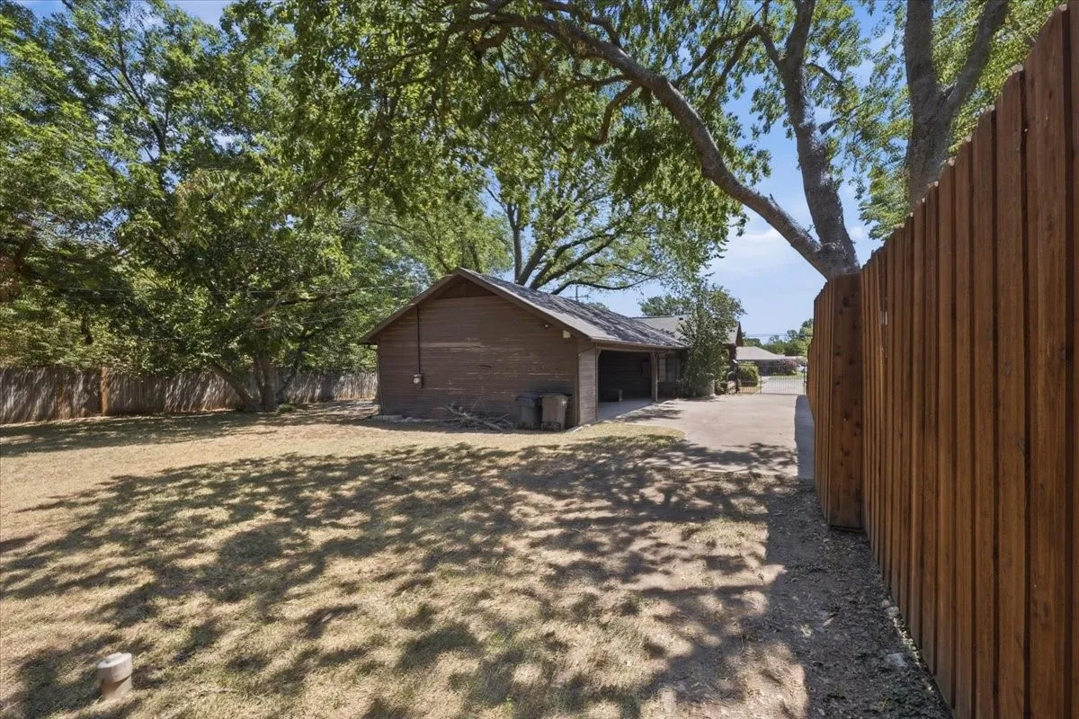 Spacious yard with mature trees, perimeter wood fencing, and a brown wood-paneled exterior structure