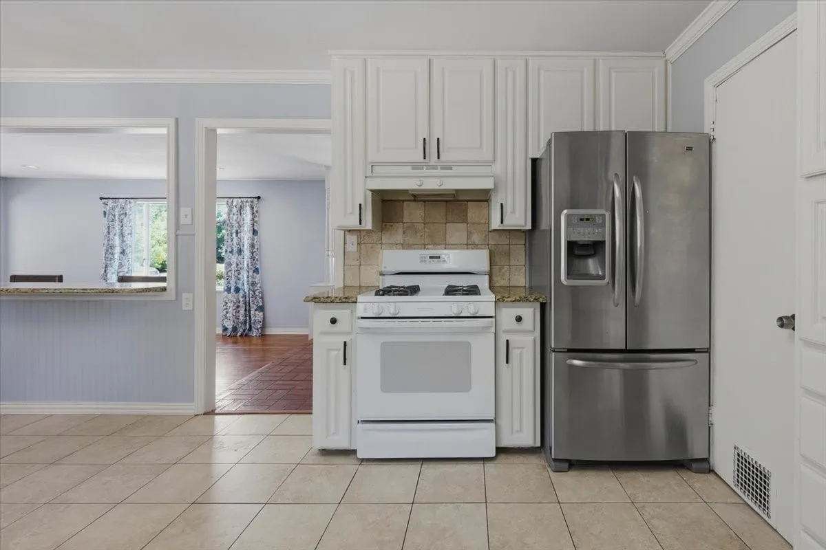 Kitchen featuring light-toned tile flooring, white cabinetry with dark hardware, a stainless steel French door refrigerator, and a gas range