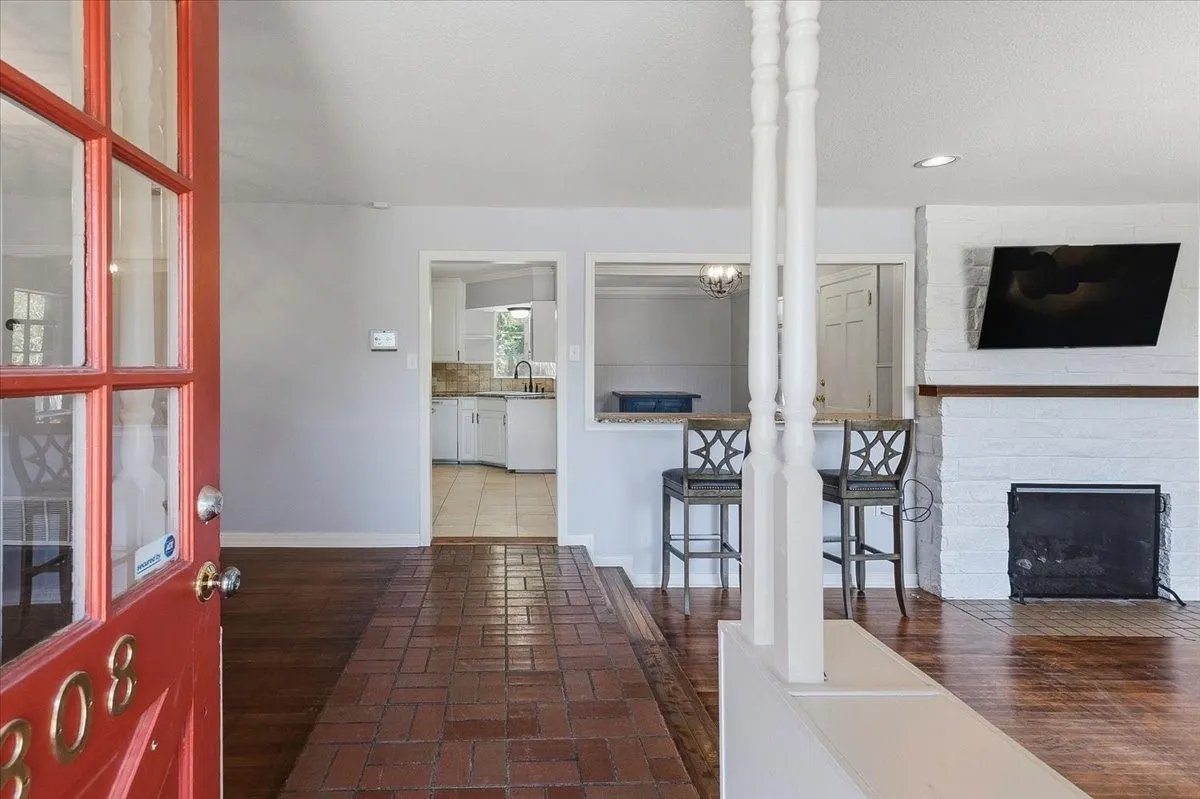 Open-concept living area featuring rich wood-finish flooring, a gas fireplace with brick surround, and a kitchen pass-through with coordinating bar seating