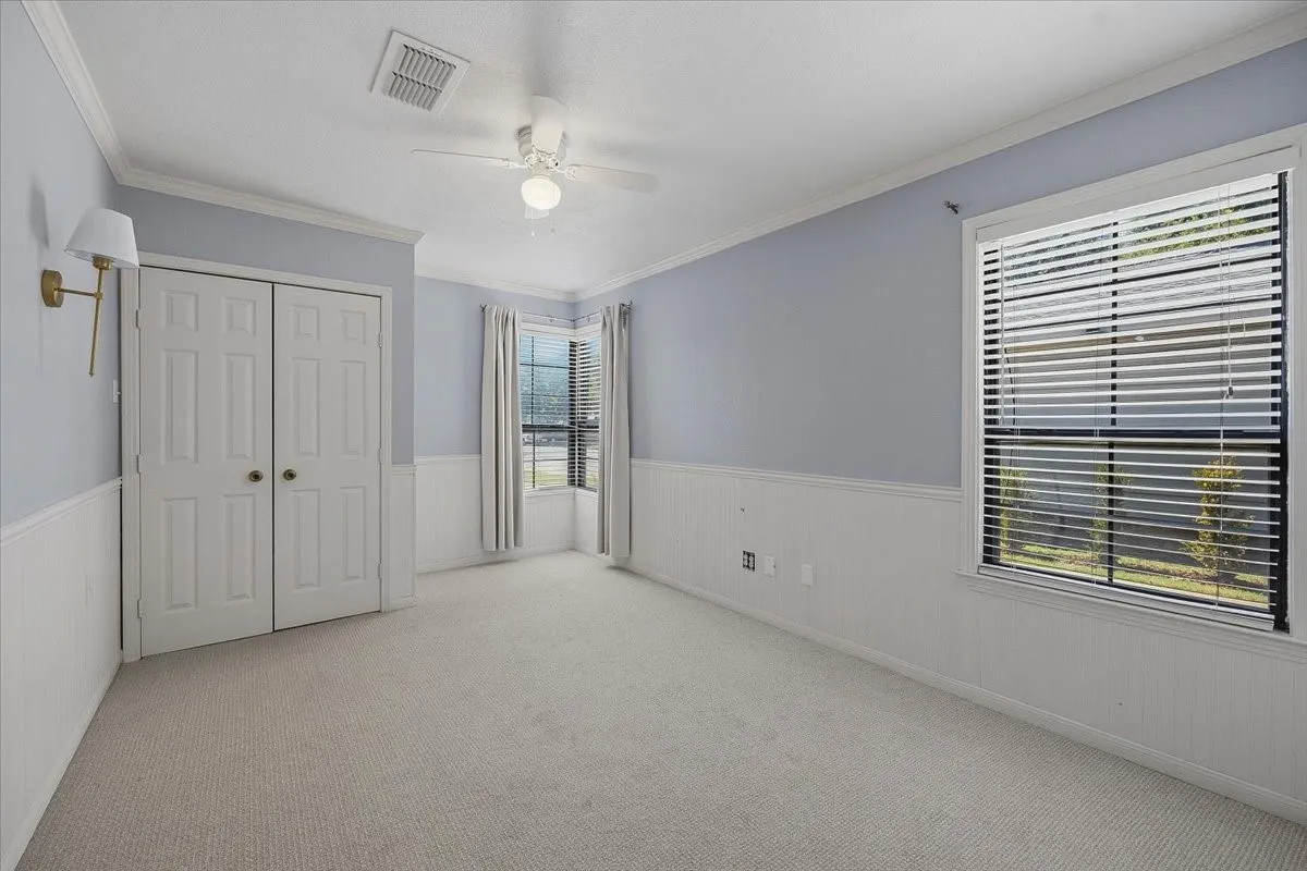Wall-to-wall carpeting, dual windows with blinds, a ceiling fan with integrated lighting, and a dual-door built-in closet