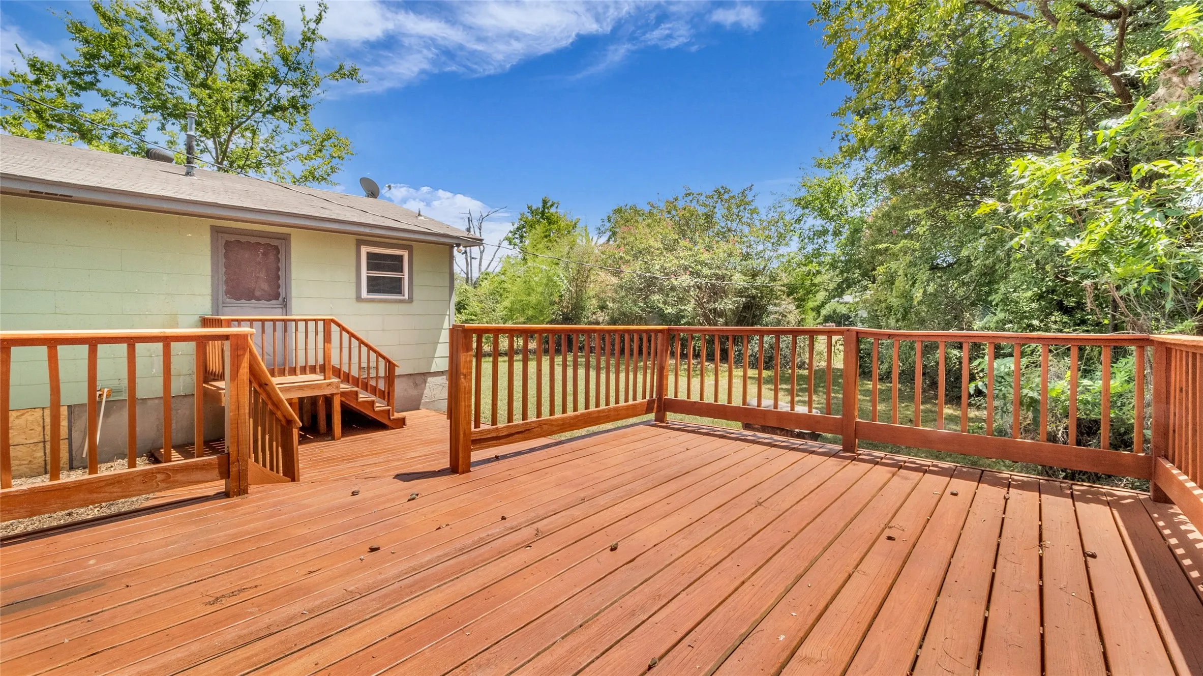 Expansive wood deck with wood railings and steps, featuring a light green exterior wall