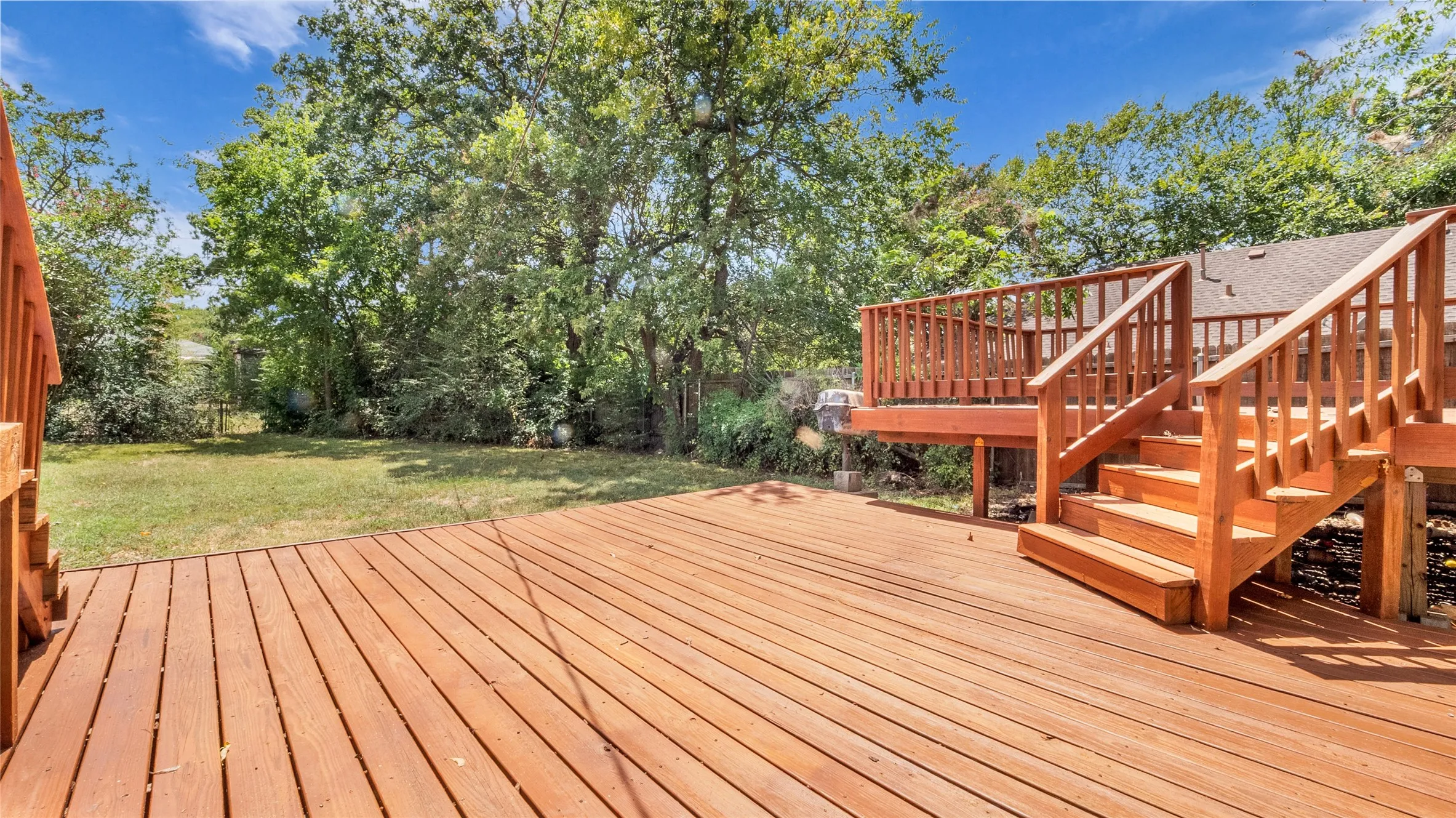 Expansive backyard featuring a natural wood-finish deck with integrated stairs and railing, and a sizable grass area