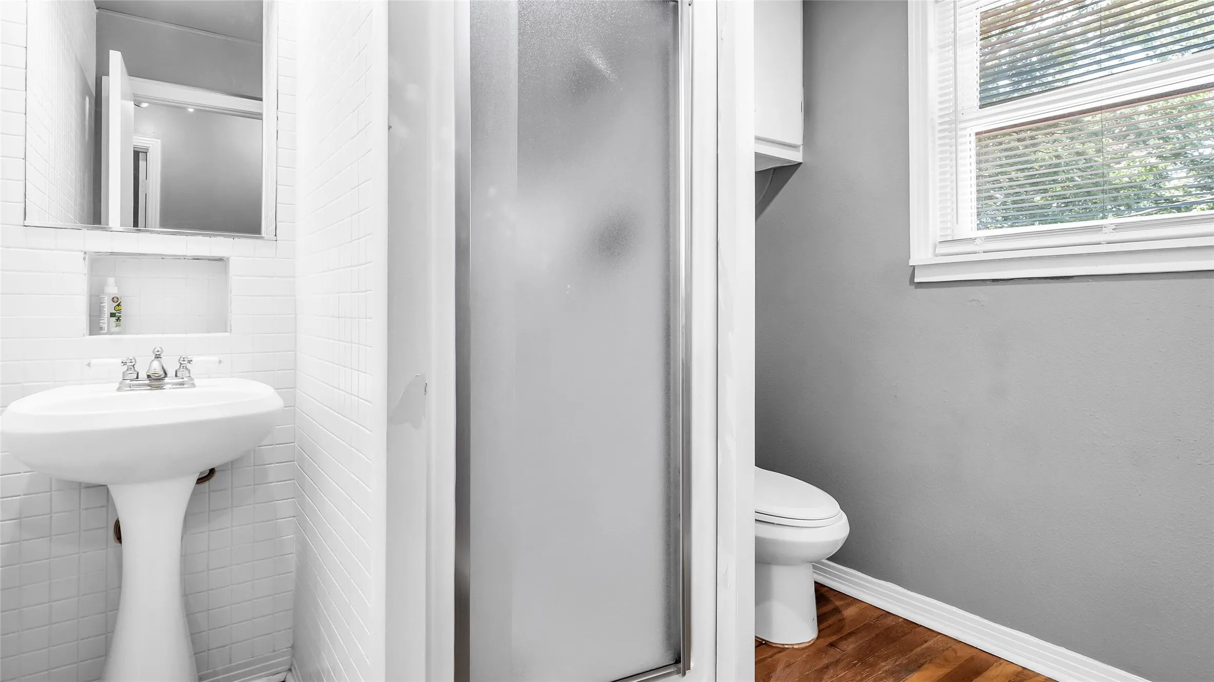 Pedestal sink with chrome faucet, tiled wall, recessed wall niche, frosted glass shower enclosure, and wood-finish flooring