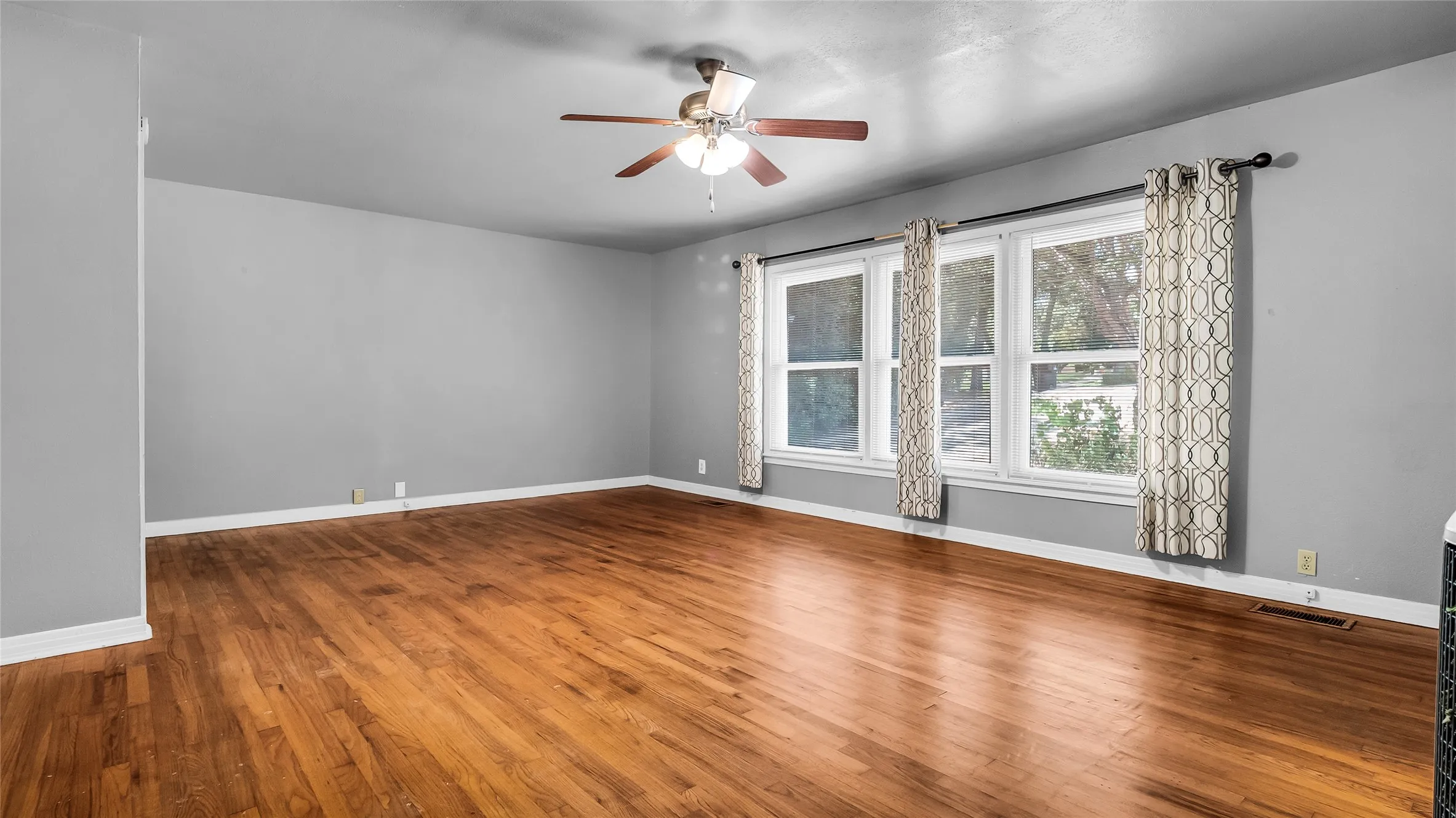 Spacious living room featuring gleaming wood-finish flooring, recessed lighting, and a ceiling fan with integrated light fixture
