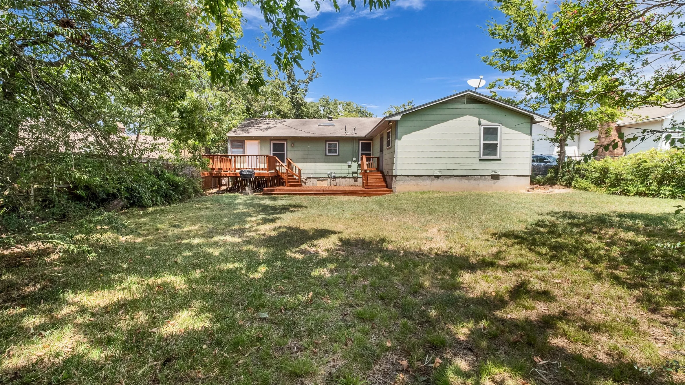 Expansive backyard featuring a manicured lawn, established perimeter trees, and a multi-level wood deck