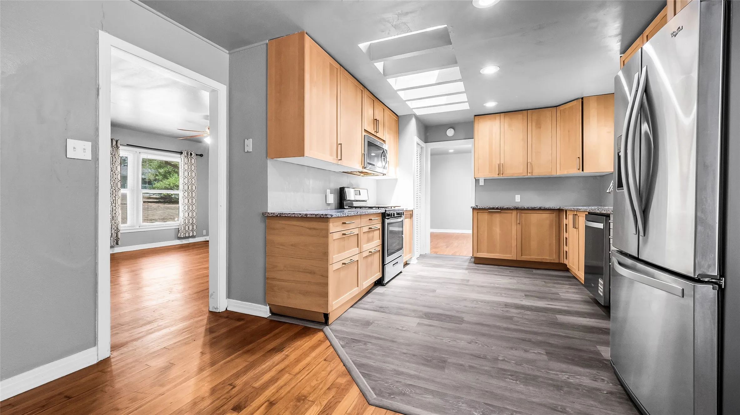 Kitchen featuring wood cabinetry, stainless steel appliances, granite countertops, and a skylight