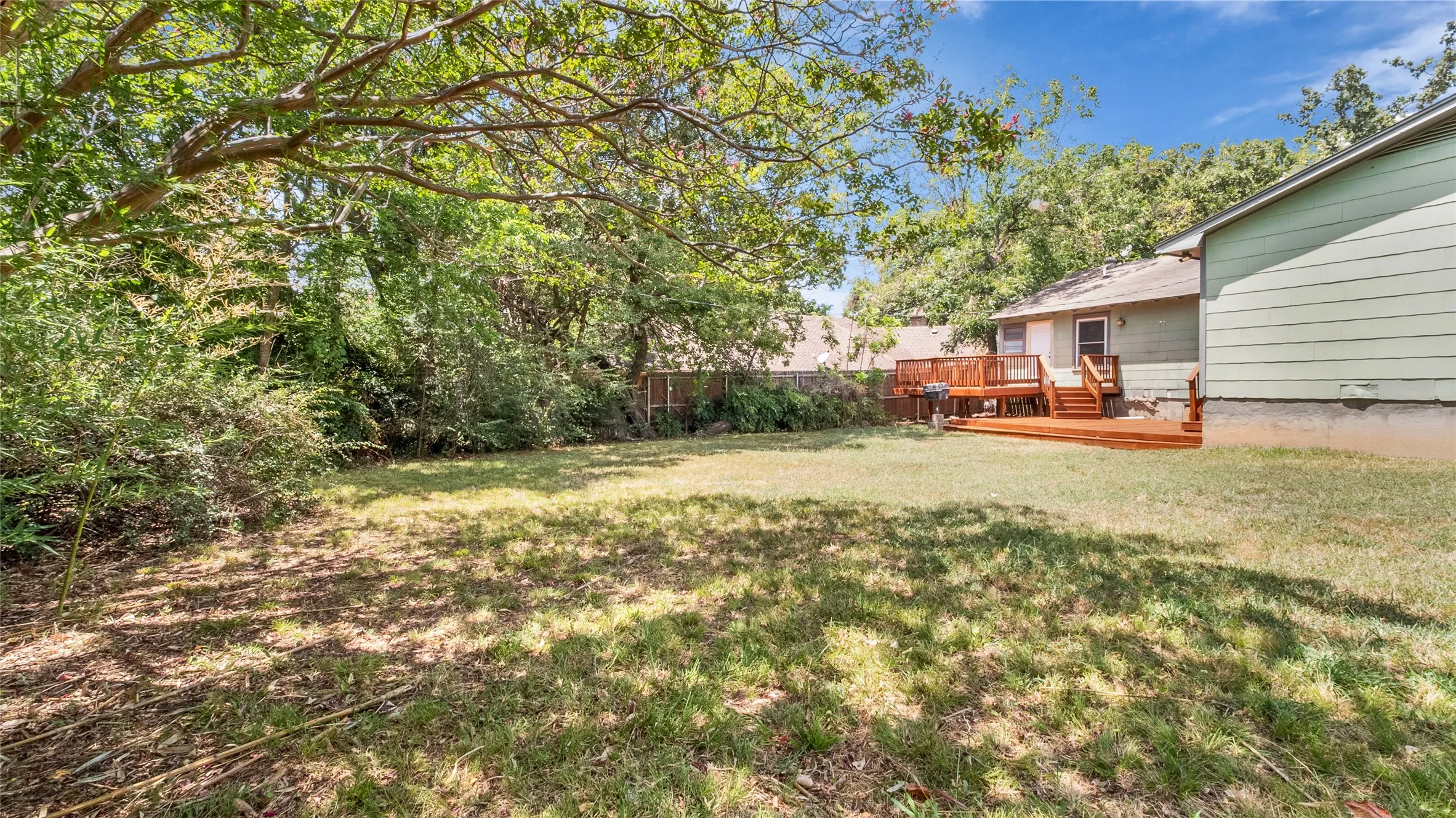 Expansive grassy yard with mature trees, wood deck, and wood privacy fencing