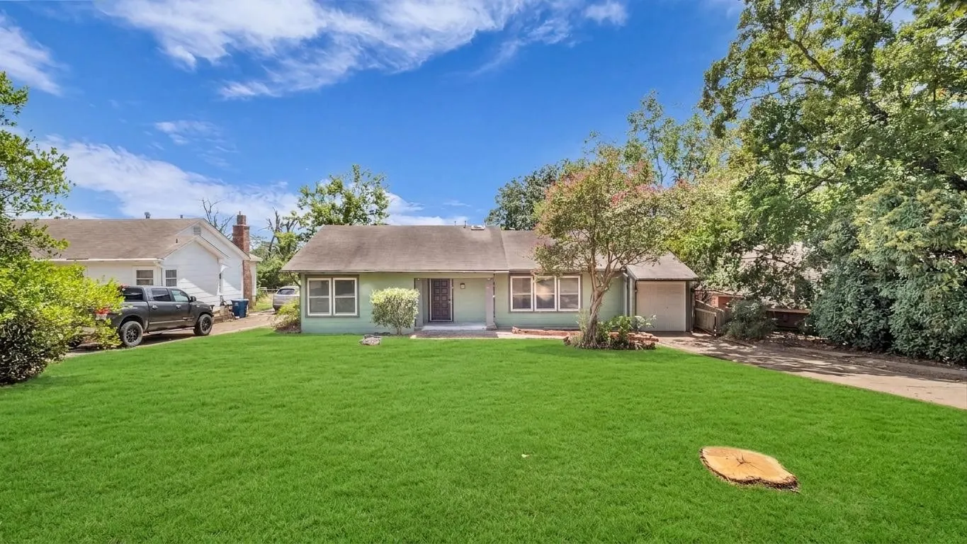 Single-story residence featuring a front lawn, mature trees, an attached garage, and a concrete driveway