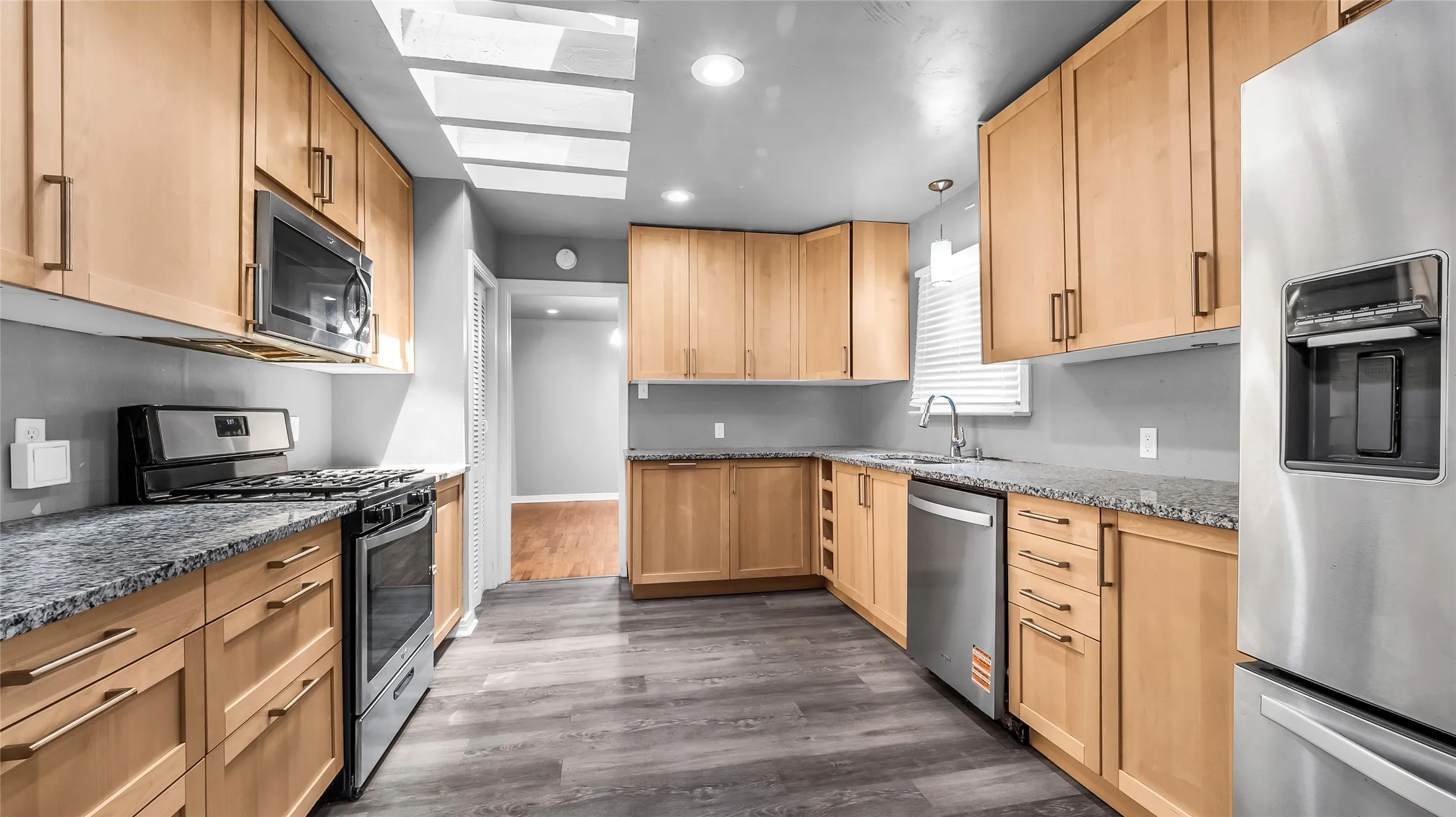 Kitchen featuring wood-finish cabinetry, stainless steel appliances, speckled countertops, and wood-finish flooring