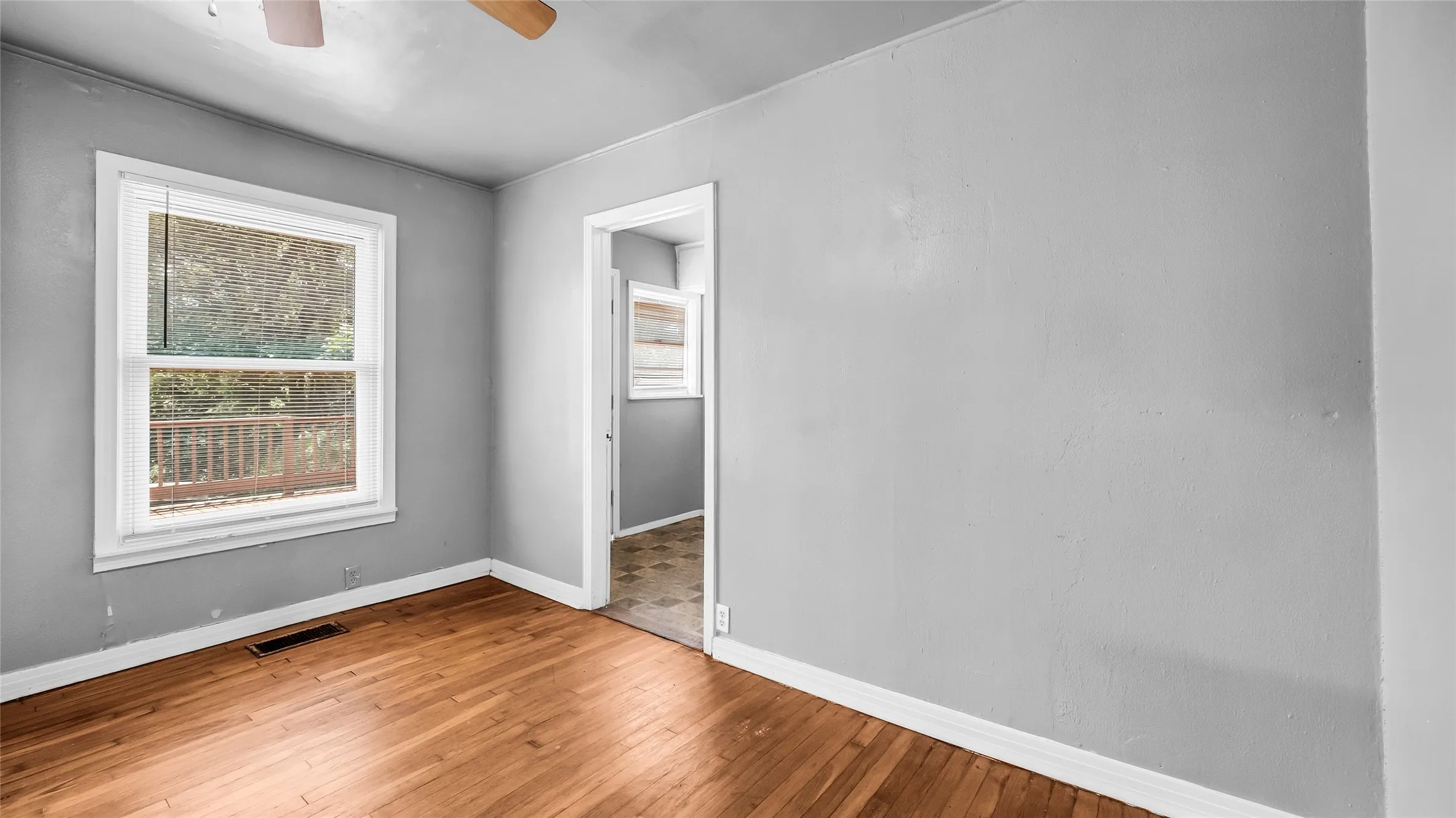 Wood-finish flooring with white trim, a window with white casing, and a ceiling fan