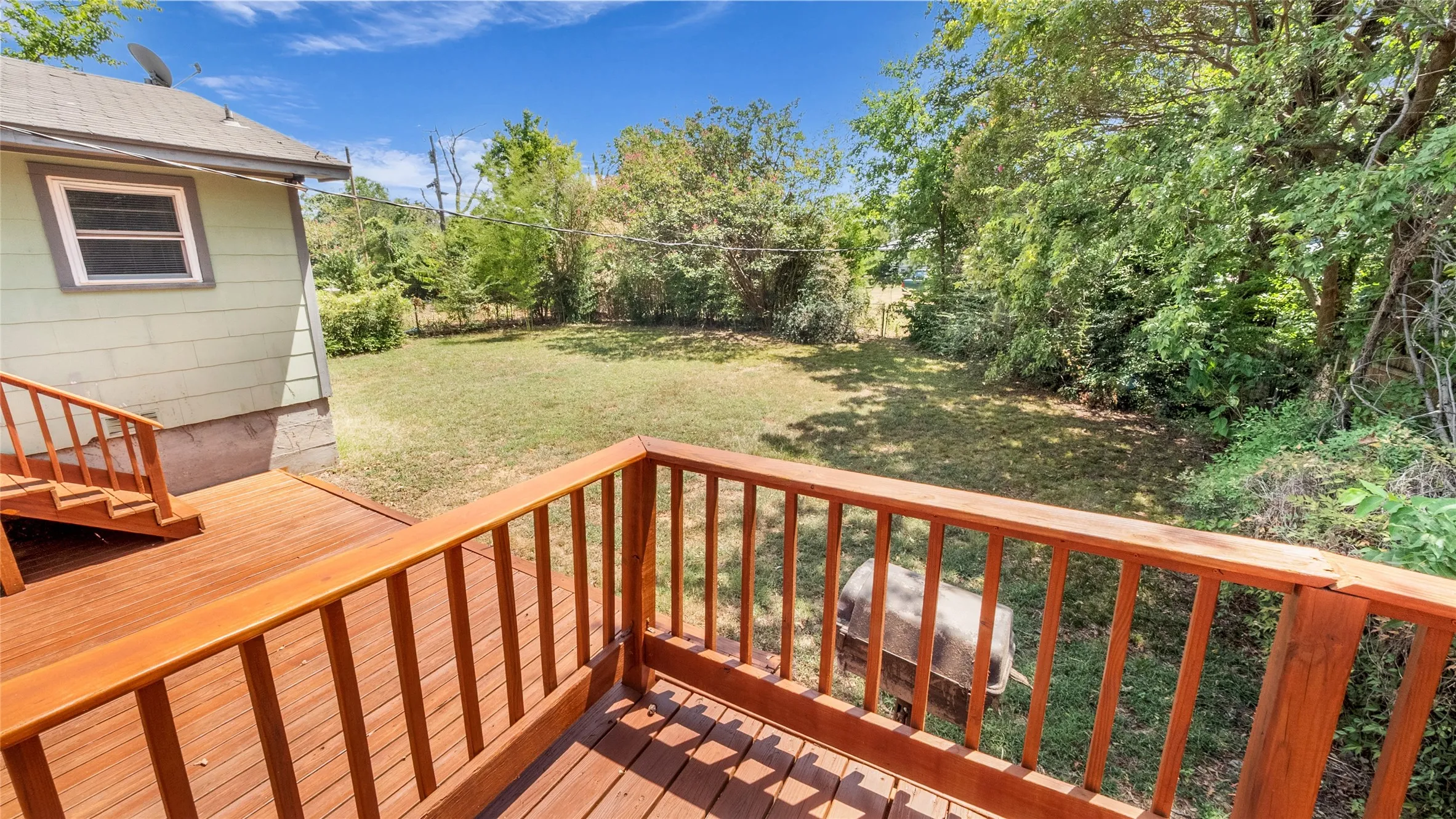 Wood deck with railings and stairs, offering access to the expansive yard space