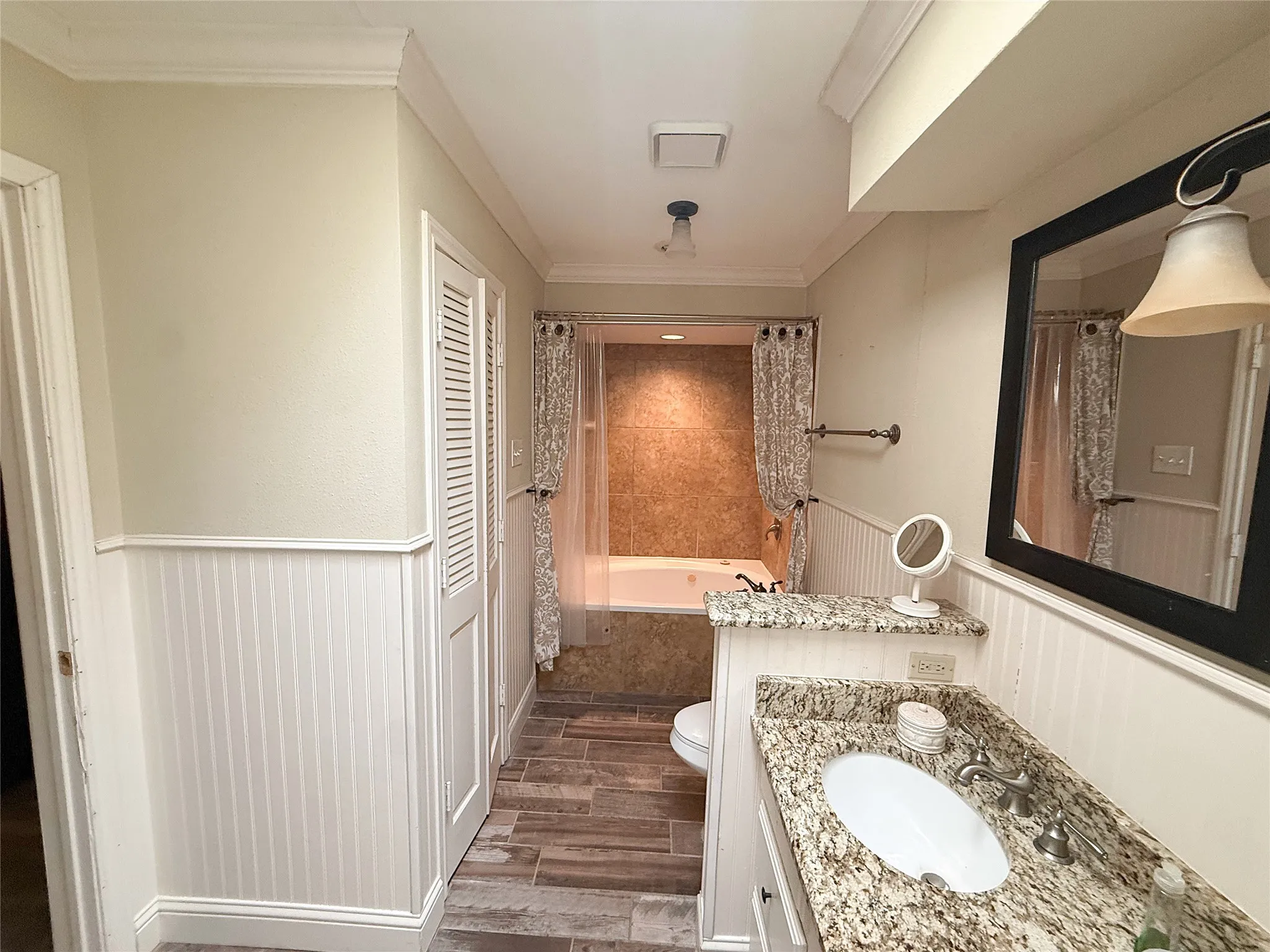 Bathroom featuring a single vanity with stone-finish countertop, white beadboard wainscoting, and wood-look tile flooring