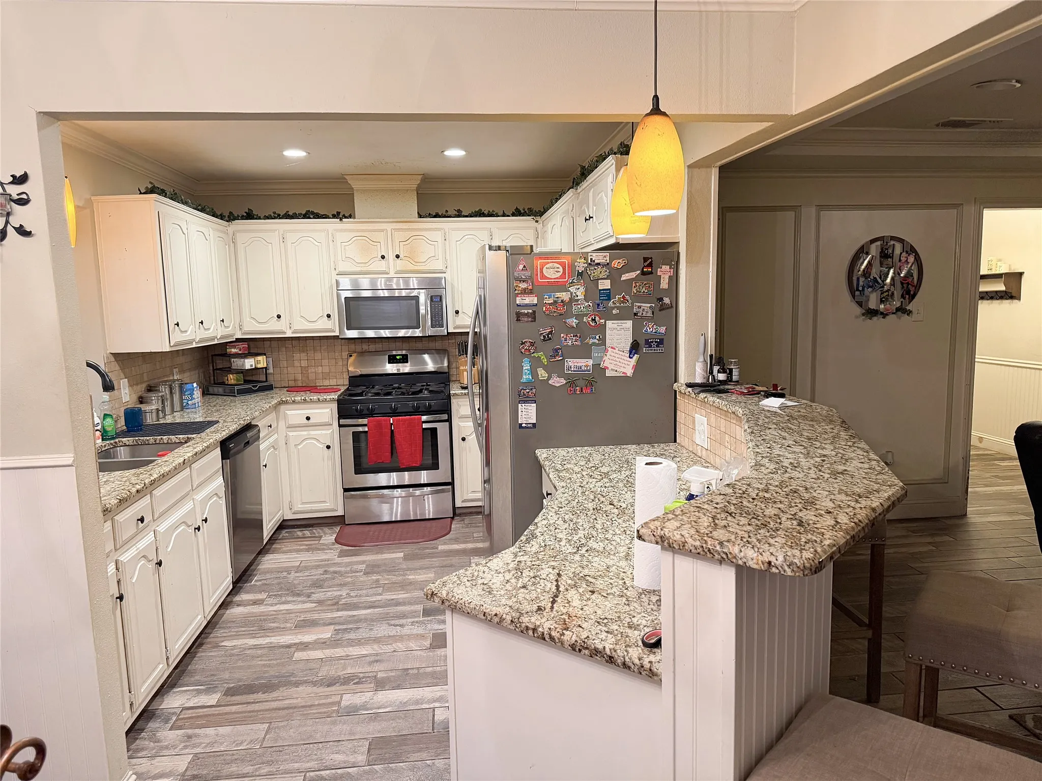 Kitchen featuring granite countertops, wood-finish flooring, white cabinetry, stainless steel appliances, and a breakfast bar