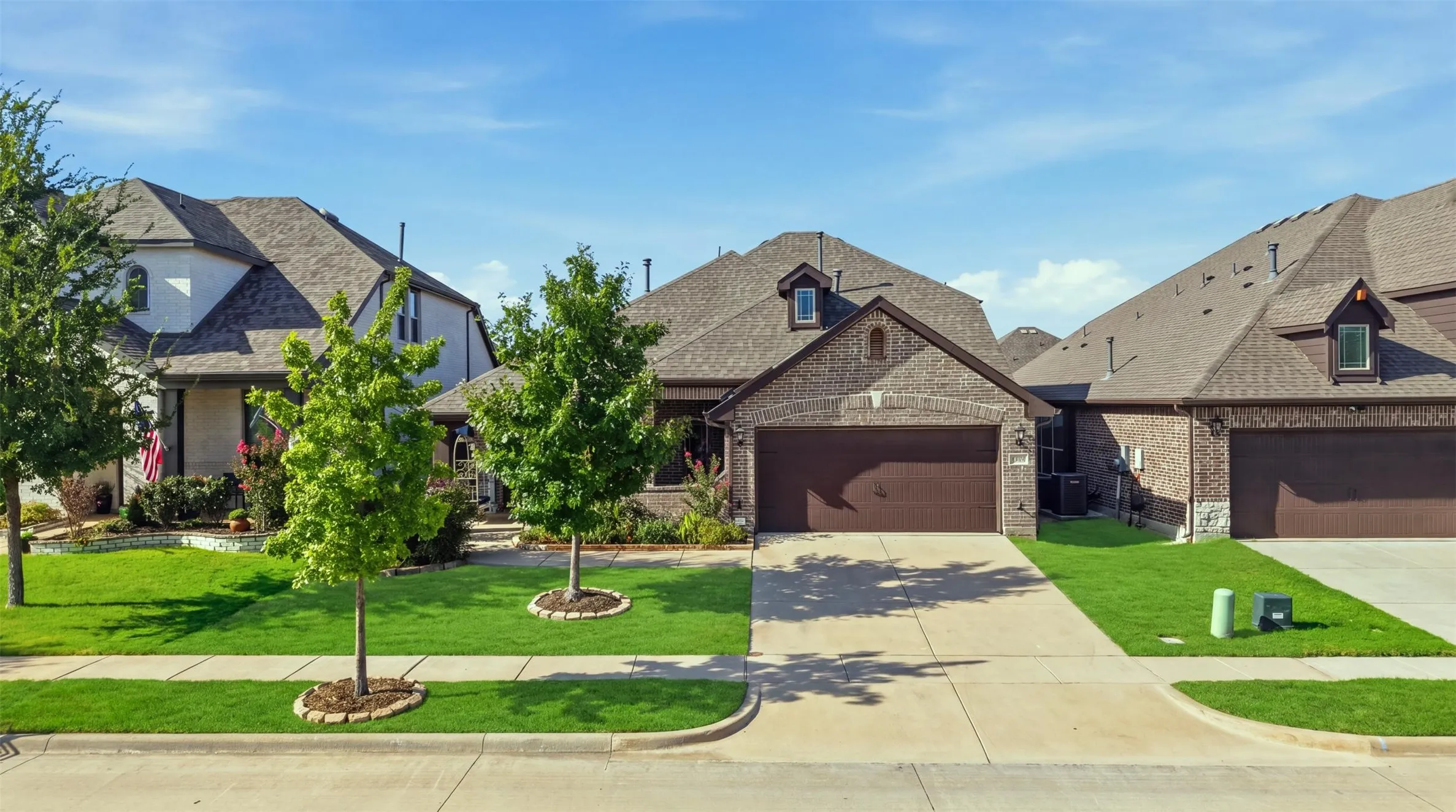 Inviting brick exterior with stone accents, an attached two-car garage, concrete driveway, and manicured landscaping that enhance the home's polished curb appeal