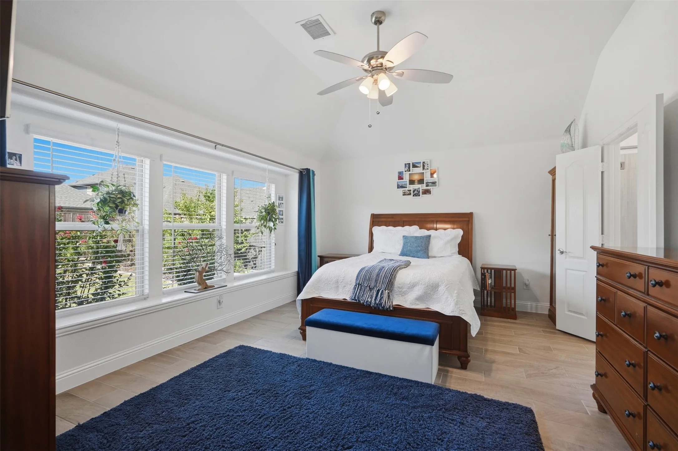 Three large windows fill the room with natural light, while wood-finish flooring, white walls, and a vaulted ceiling create a spacious, inviting retreat