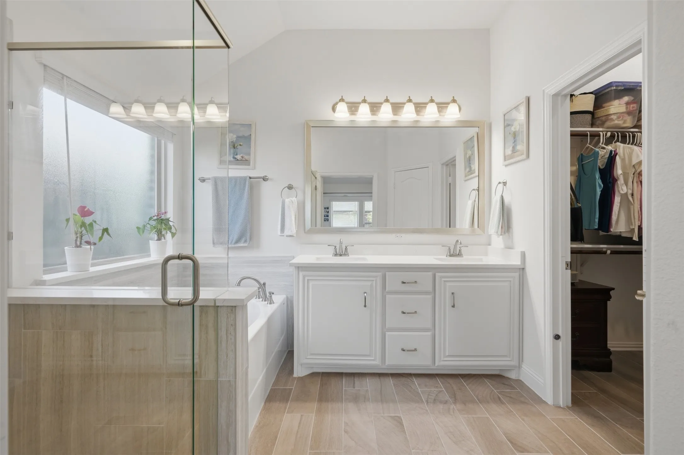 A double vanity with crisp white cabinetry pairs with a large framed mirror, while a soaking tub and glass-enclosed walk-in shower create a relaxing retreat