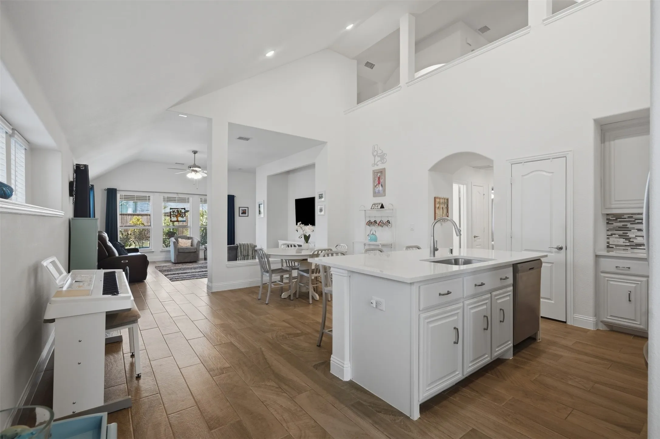 Well-appointed kitchen featuring a spacious island with an undermount sink, crisp white cabinetry, stainless steel dishwasher, and warm wood-finish flooring for a clean, inviting look