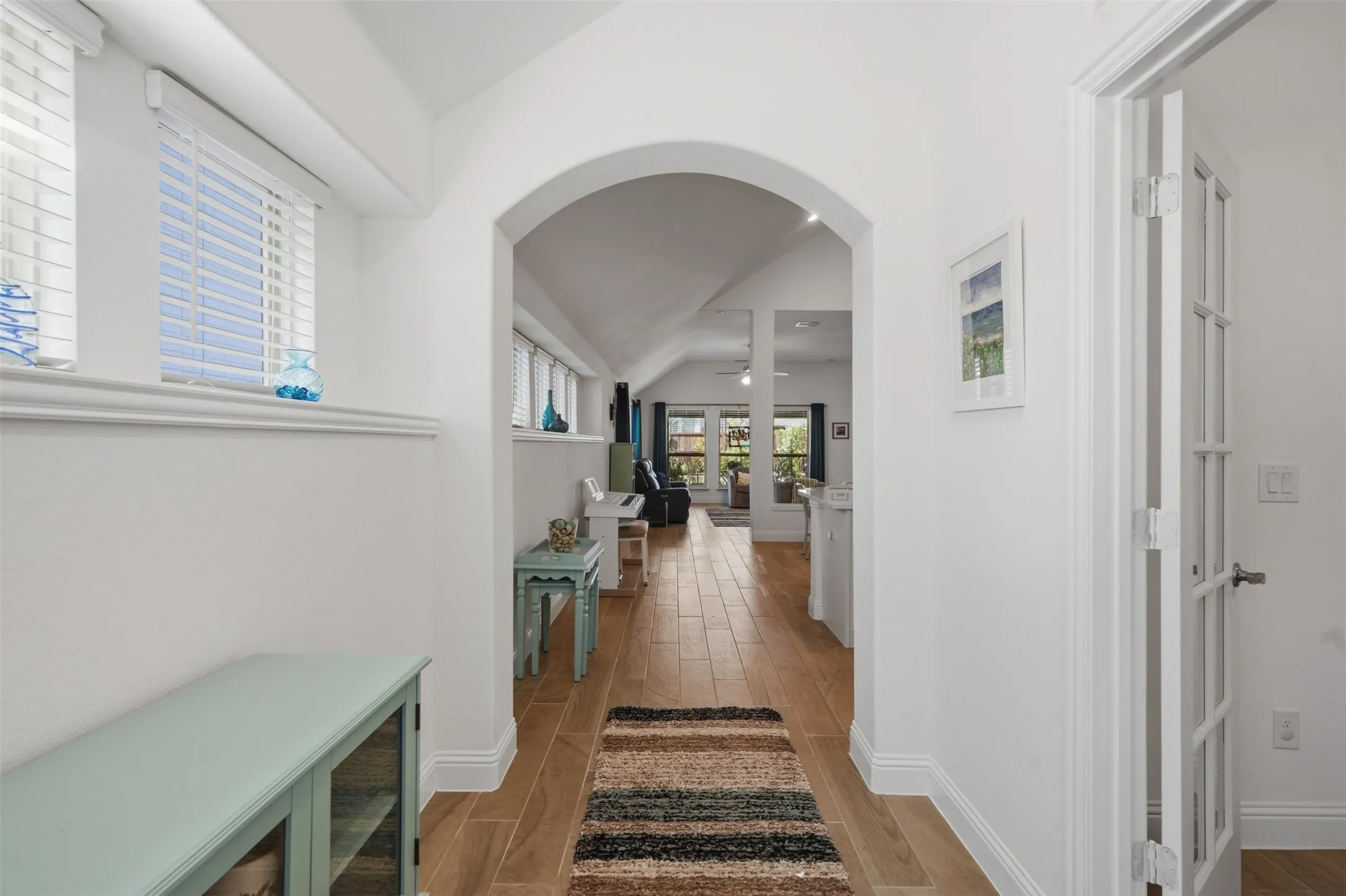 Warm wood-finish flooring, crisp white trim, and an elegant arched entry create a polished look, complemented by a charming French door with glass panels