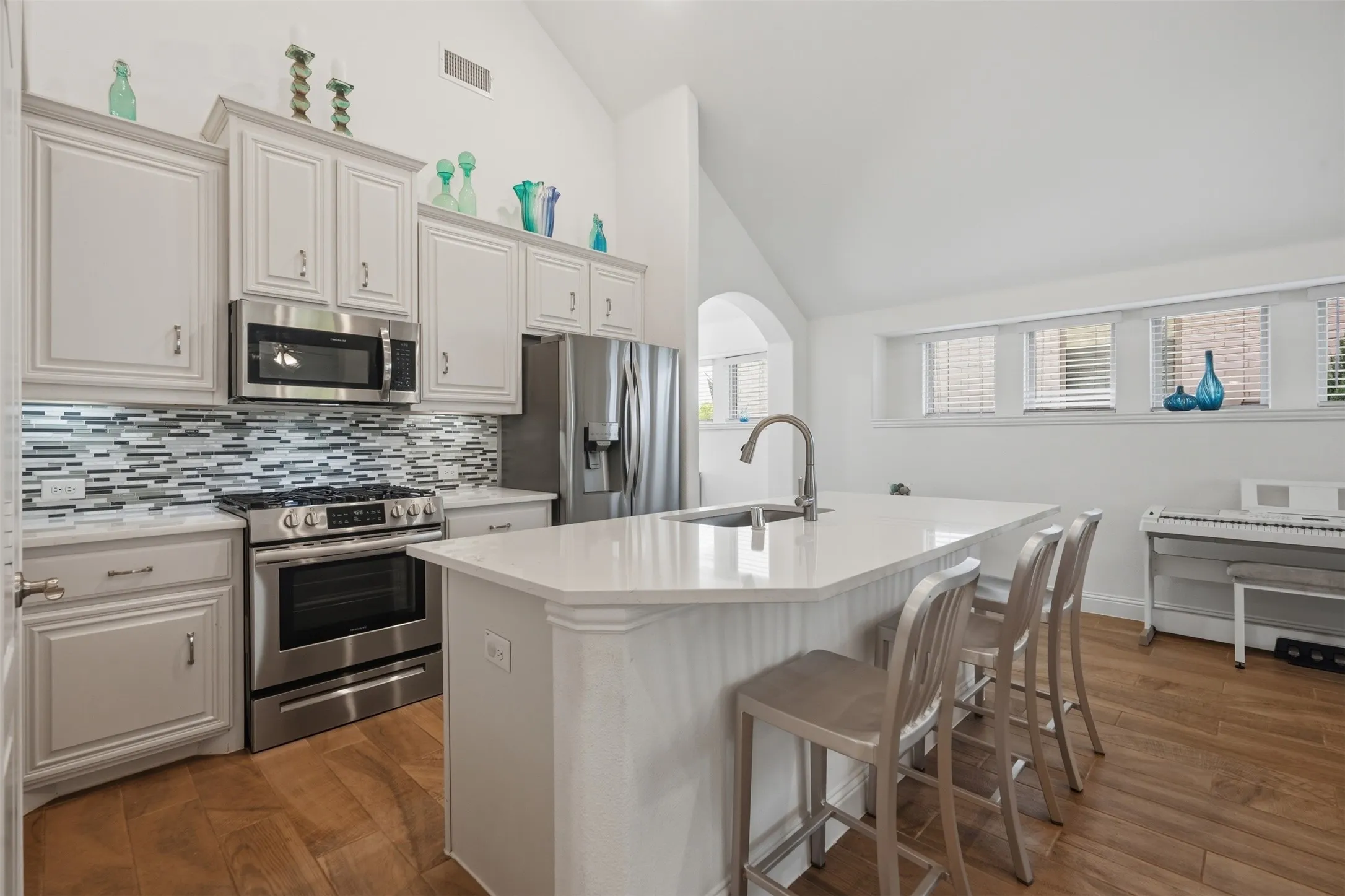 Stylish white shaker cabinetry, stainless steel appliances, and a mosaic tile backsplash surround a spacious center island with seating, all complemented by warm wood-finish flooring